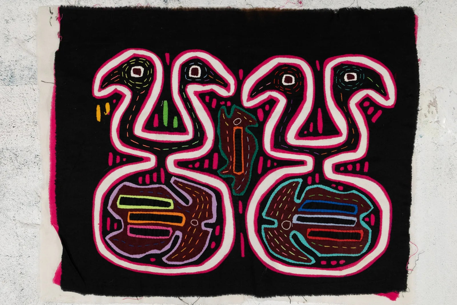 Hand-stitched black tapestry featuring colorful geometric patterns of animals in pink, green, and orange designs.