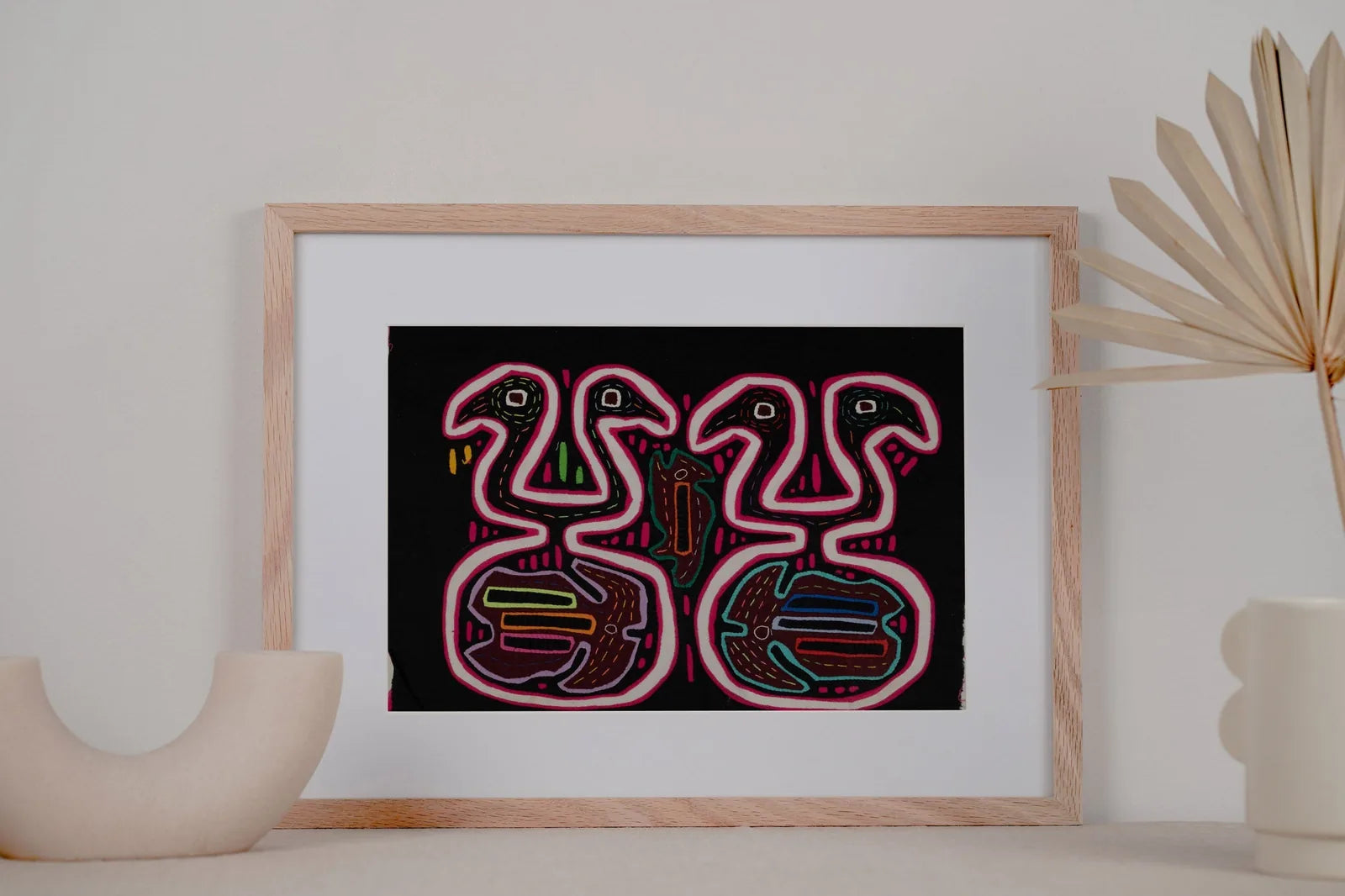 Black and pink optical illusion Mola tapestry featuring abstract animal shapes on a black background, framed decoratively.