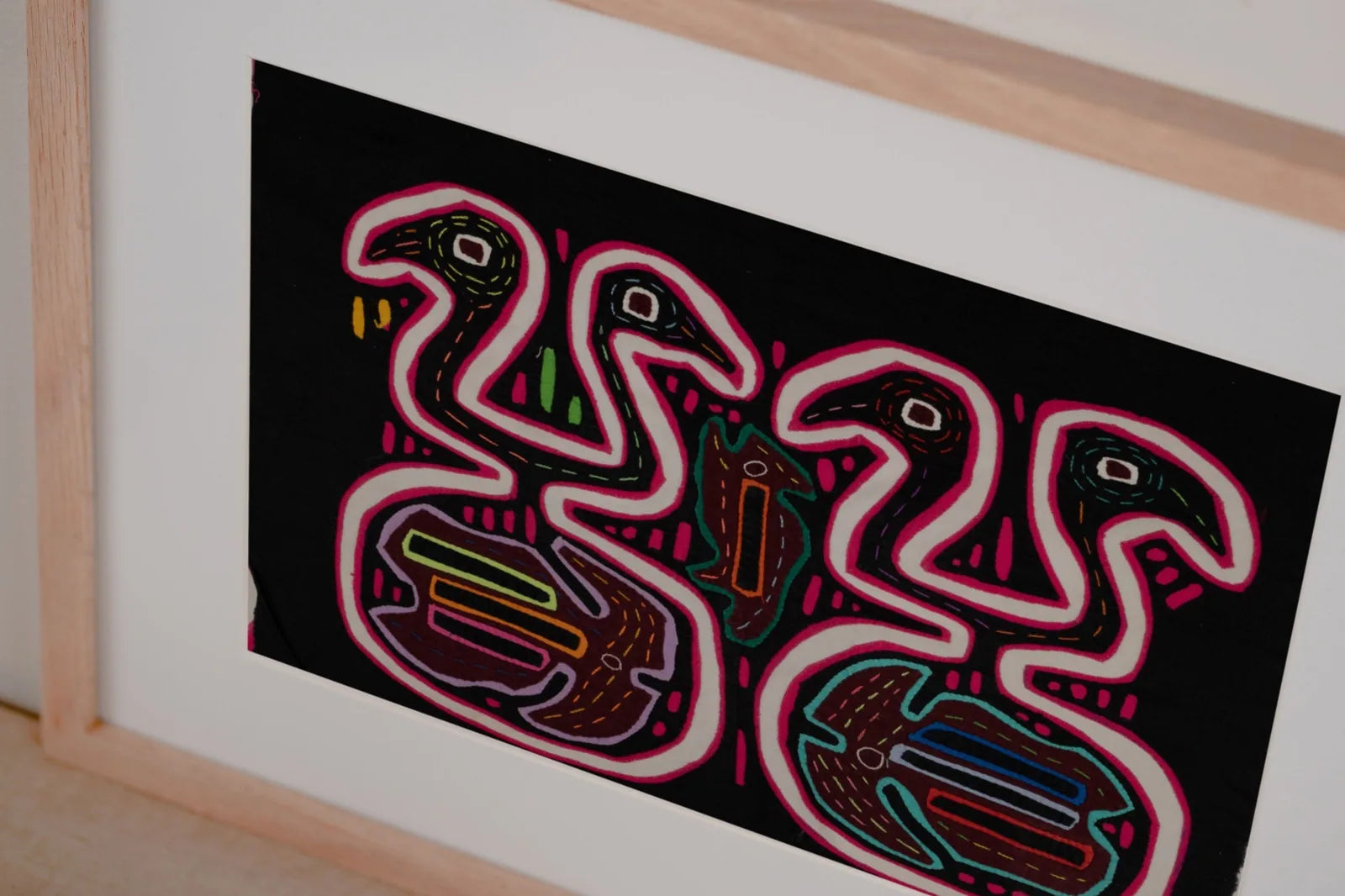 Colorful black and pink optical illusion design featuring stylized figures, framed as a decorative tapestry.