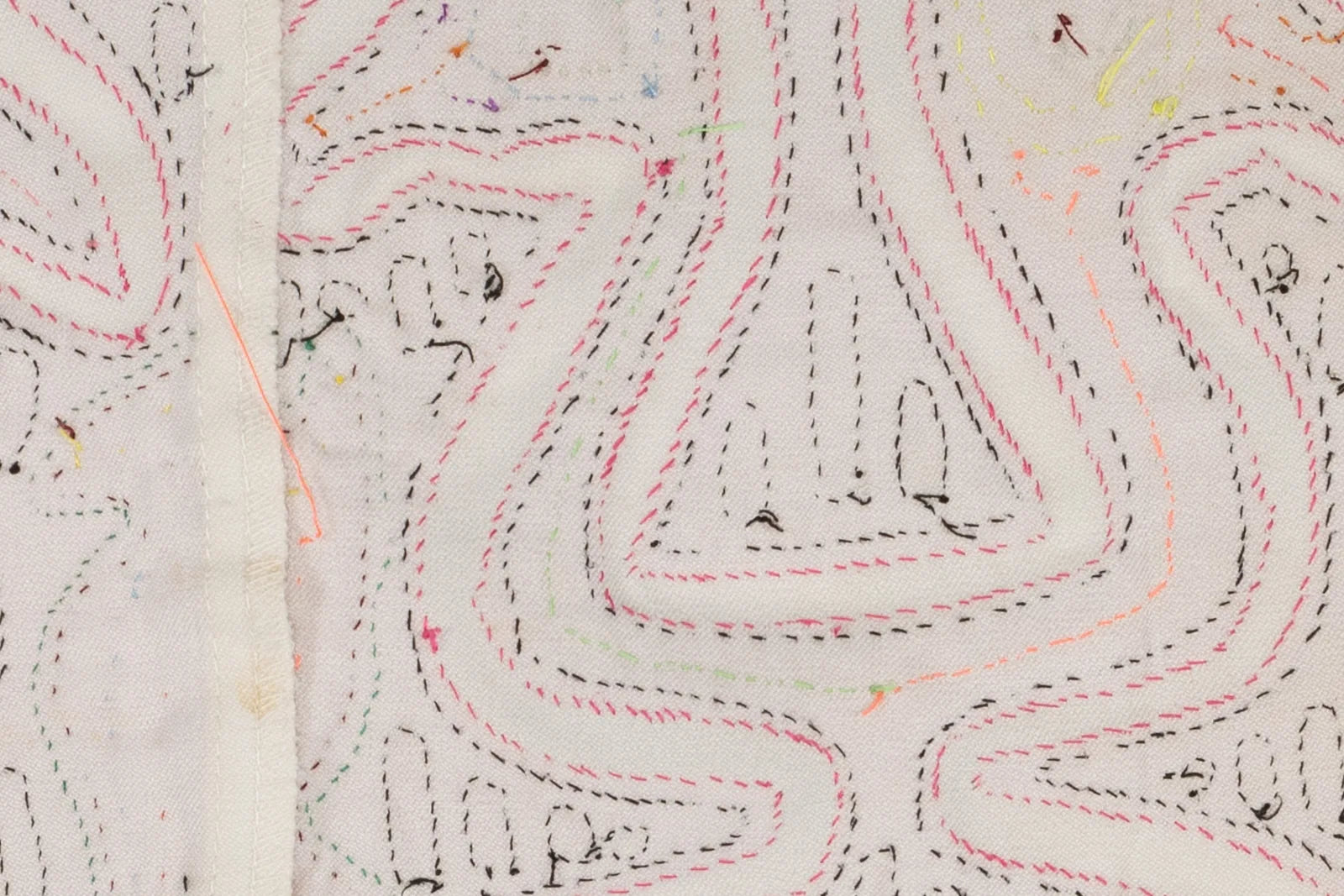 Hand-stitched Mola textile featuring pink and black geometric patterns on a white background. Unique and colorful design.