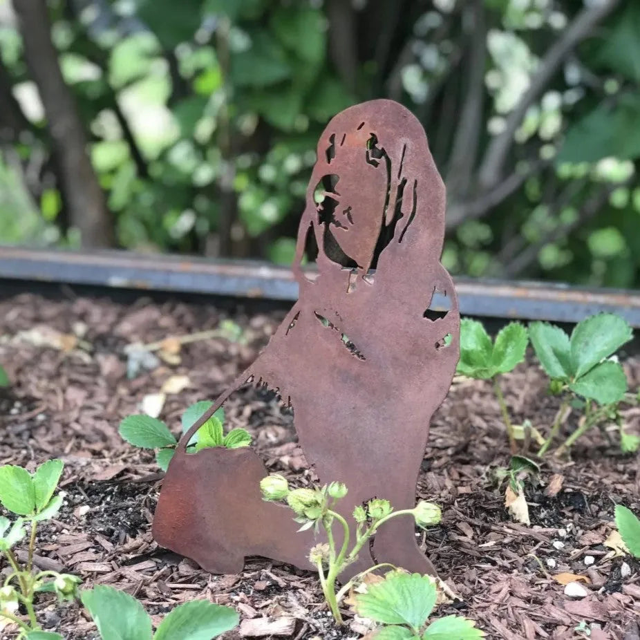 Rusty Corten steel Bloodhound silhouette accentuates a garden, surrounded by vibrant green plants and mulch.