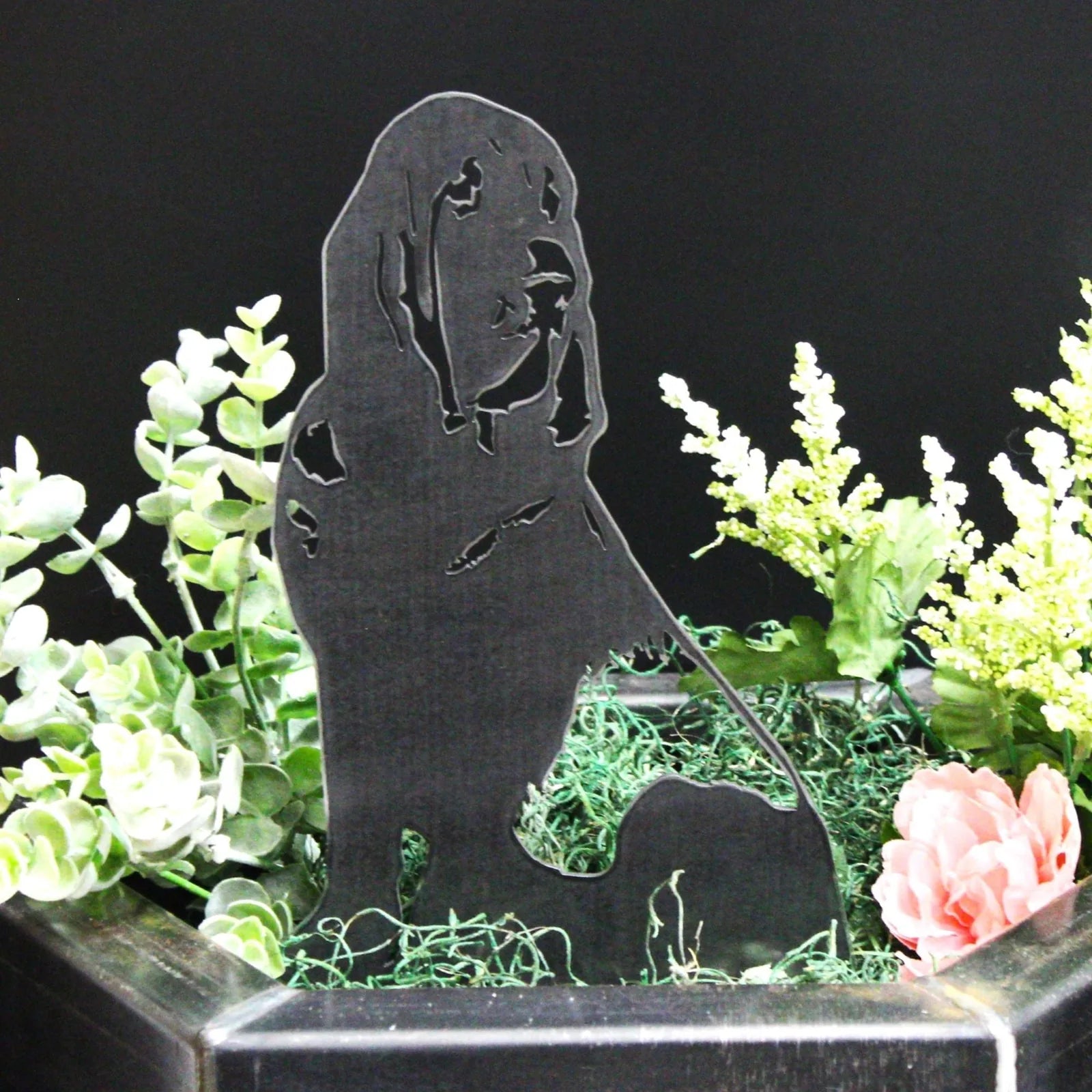 Black metal silhouette of a Bloodhound, surrounded by greenery and artificial flowers in a decorative planter.