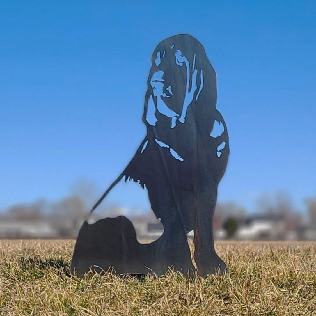 Bloodhound metal silhouette in matte black standing on grass, showcasing intricate cut-out design against a clear blue sky.