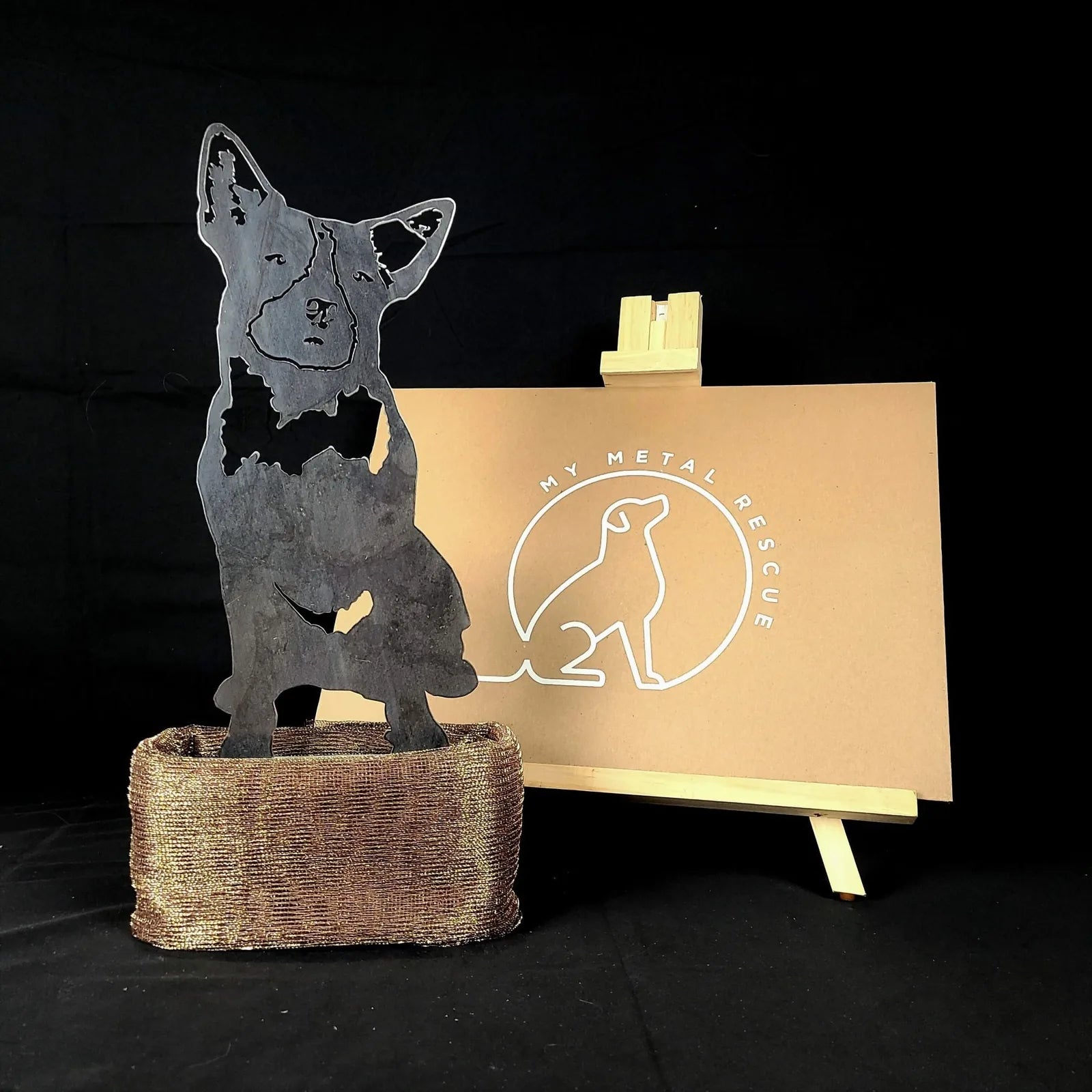 Blue Heeler metal silhouette in black, displayed on a brown woven base with a logo backdrop. Ideal for outdoor decor.