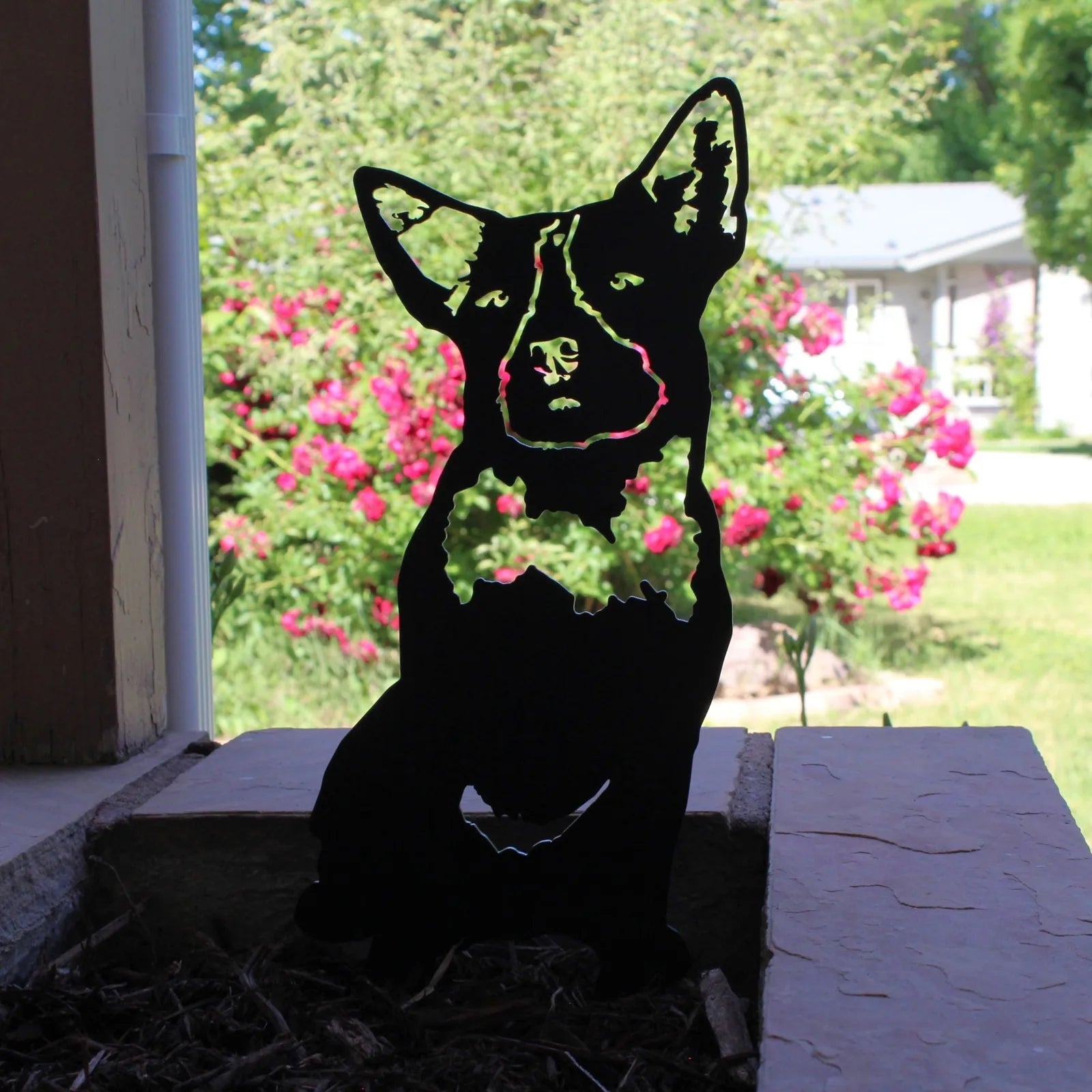 Black metal silhouette of a Blue Heeler dog, detailed with a bowtie, set against a background of blooming flowers.