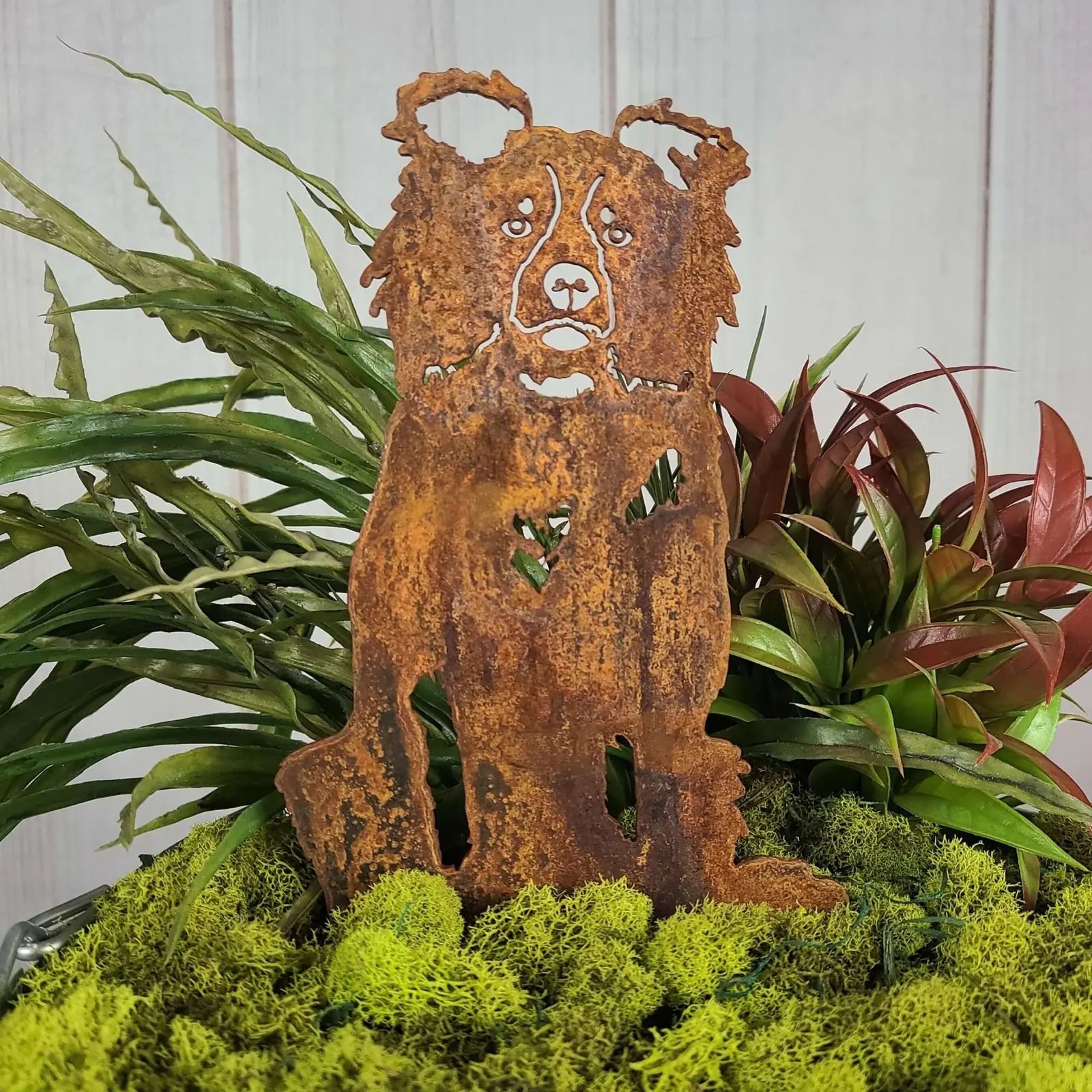 Border Collie silhouette in rusted Corten steel, placed among vibrant greenery and moss accents.