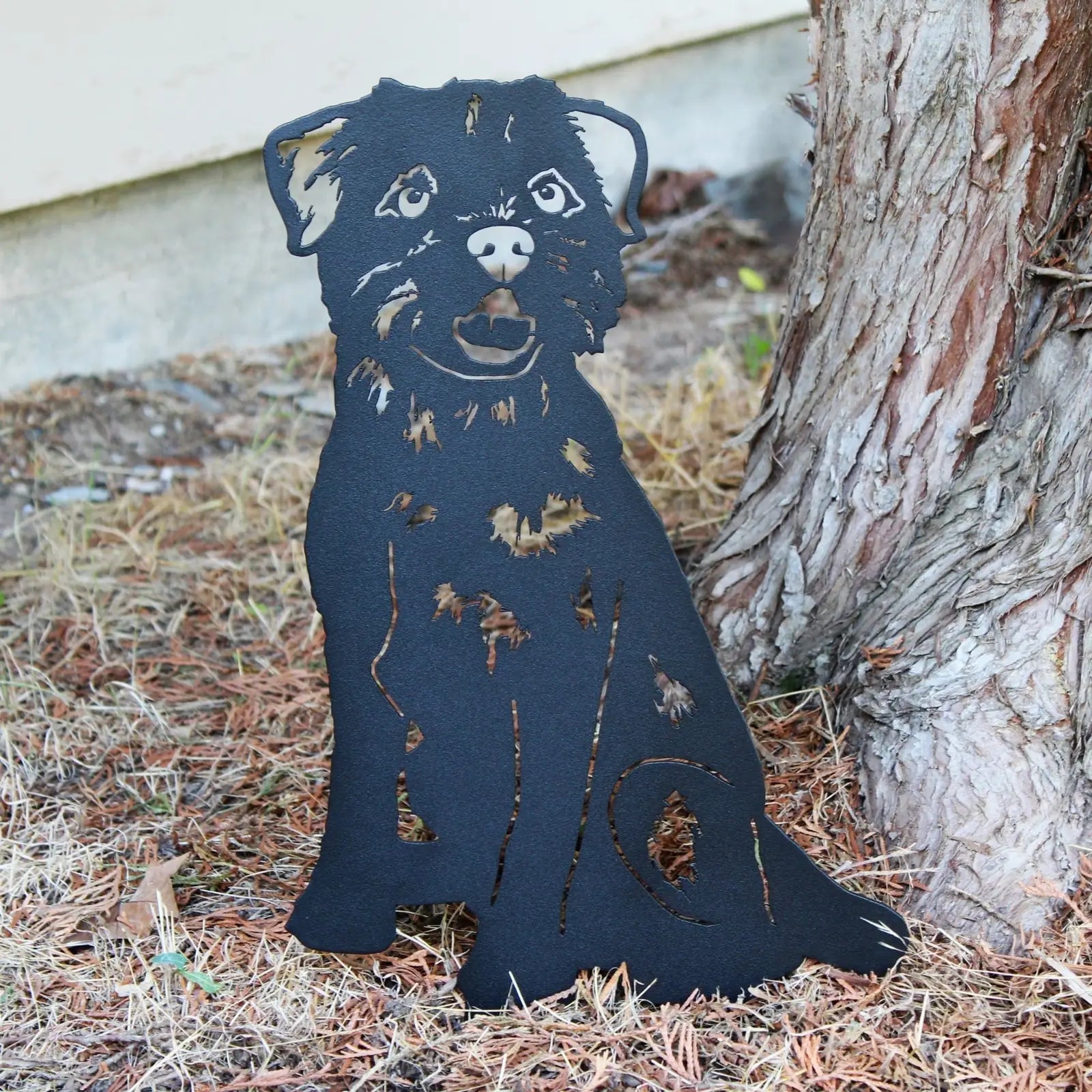 Black metal silhouette of a Border Terrier resting among pine needles, showcasing detailed cutouts and a playful expression.