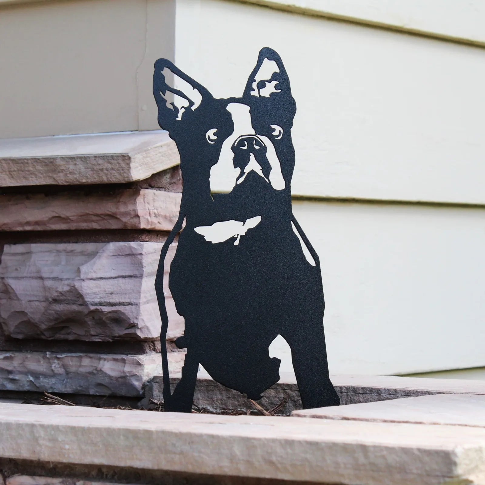 Black metal silhouette of a Boston Terrier sitting on stone steps, showcasing intricate details of the breed.