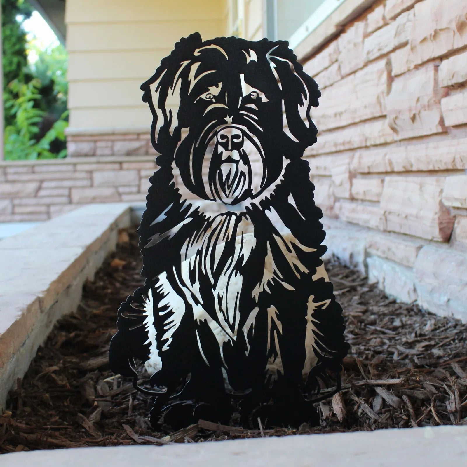 Bouvier Des Flandres metal silhouette in black, detailed design, placed in mulch near a stone wall.