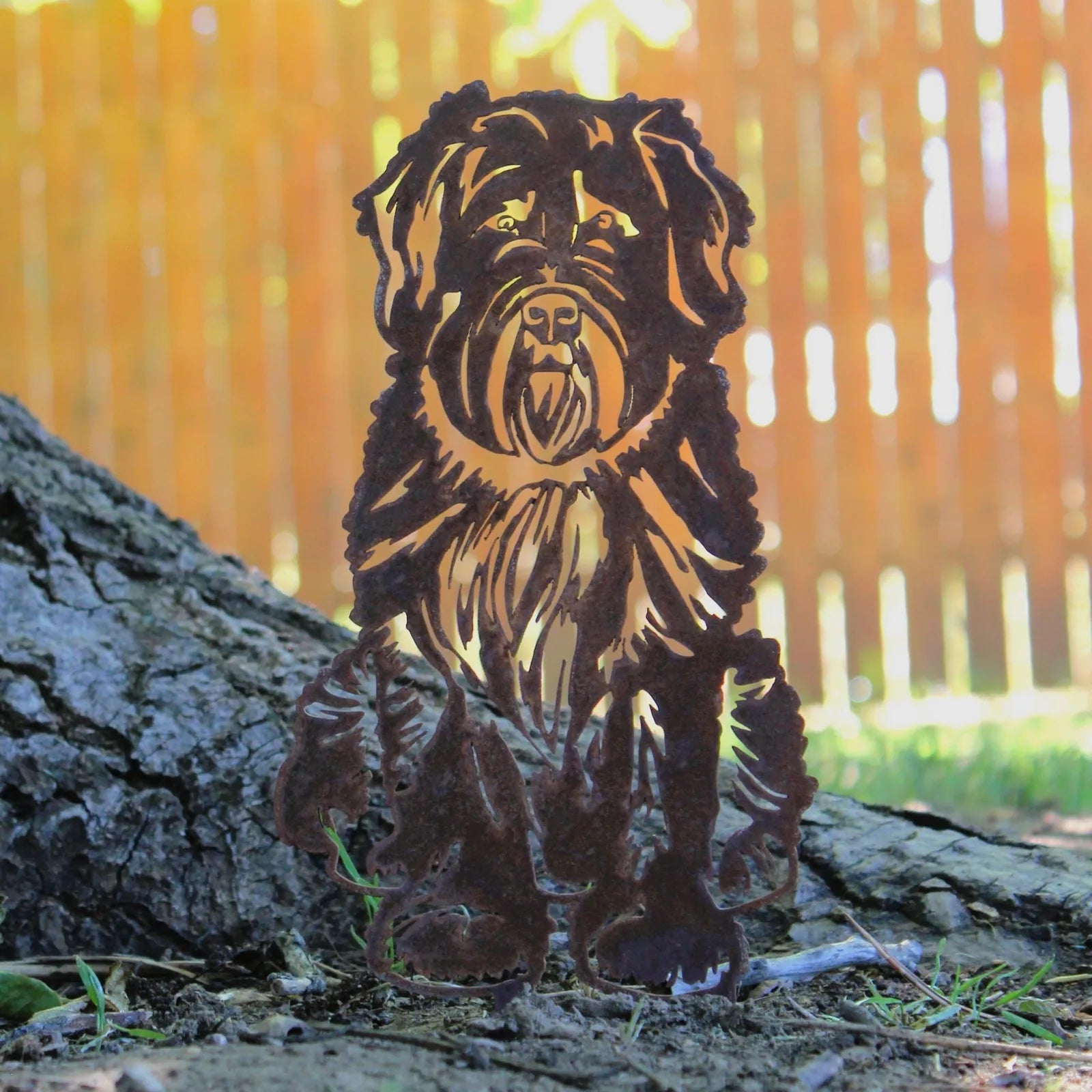 Bouvier Des Flandres metal silhouette in weathered brown, leaning against a tree with a blurred wooden fence in the backgr...