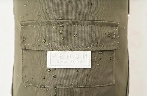 Water-resistant green dog raincoat featuring a back pocket with silicone logo and water droplets on the fabric.