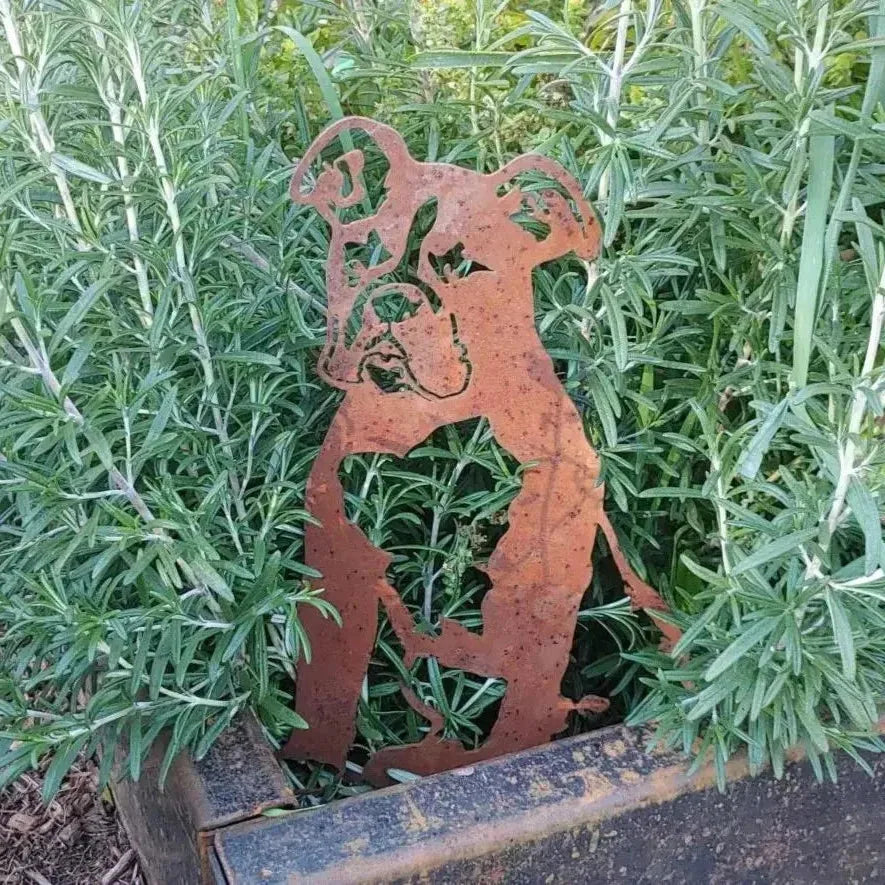 Boxer metal silhouette in rusted Corten steel surrounded by lush green plants, perfect for outdoor dog decor.