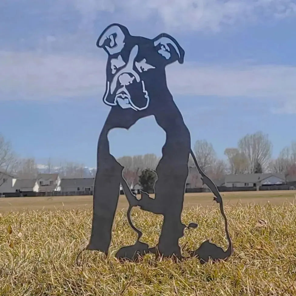 Black metal silhouette of a Boxer dog seated in a grassy field under a clear blue sky.