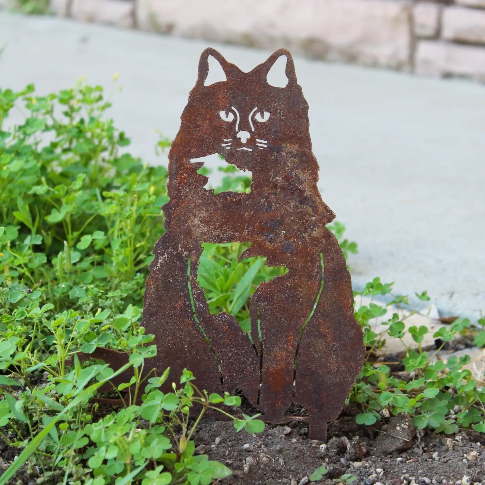 Rusty metal silhouette of a British Longhair cat, nestled among greenery, showcasing intricate cutout details.
