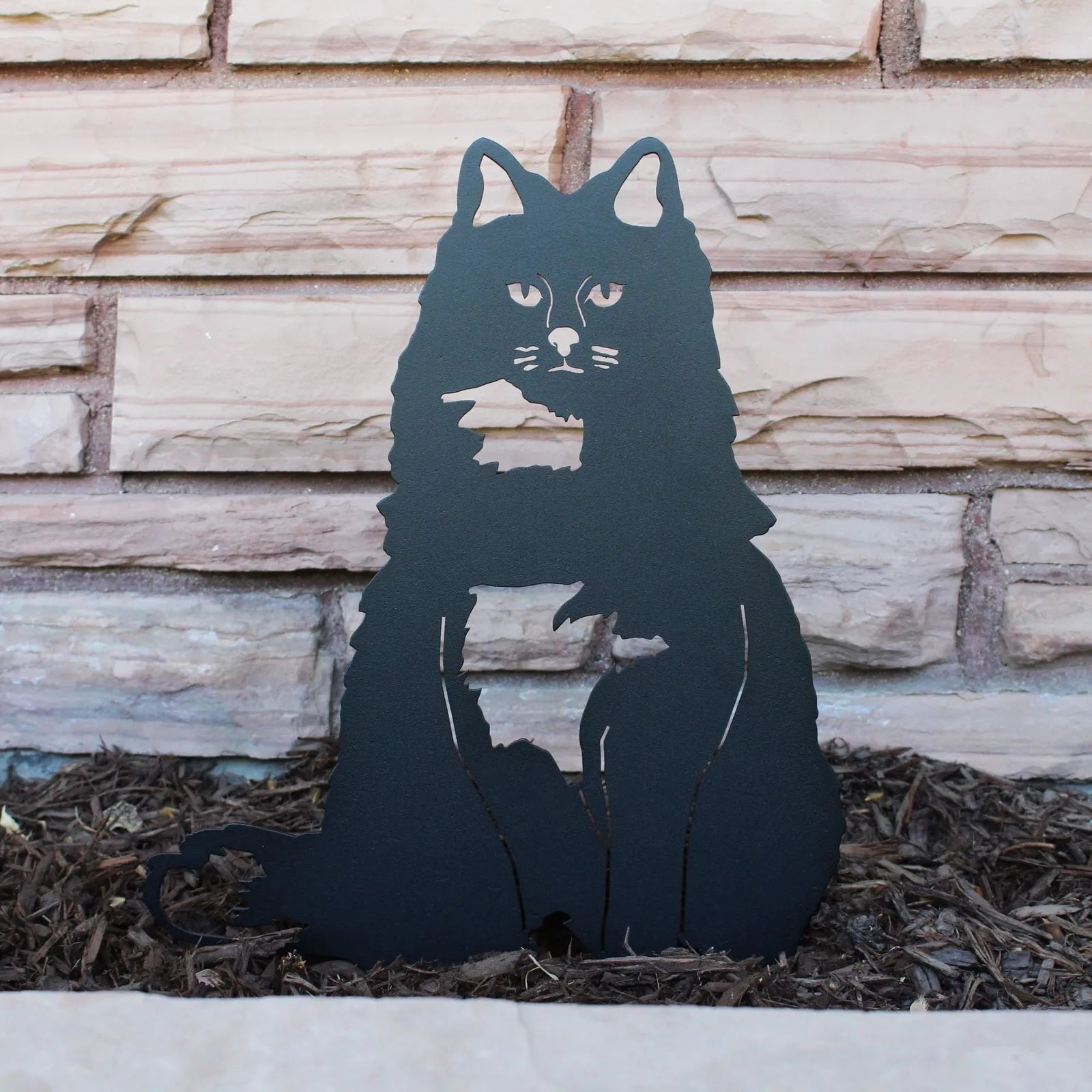 Handcrafted black metal silhouette of a British Longhair cat, set against stone, perfect for outdoor decor.
