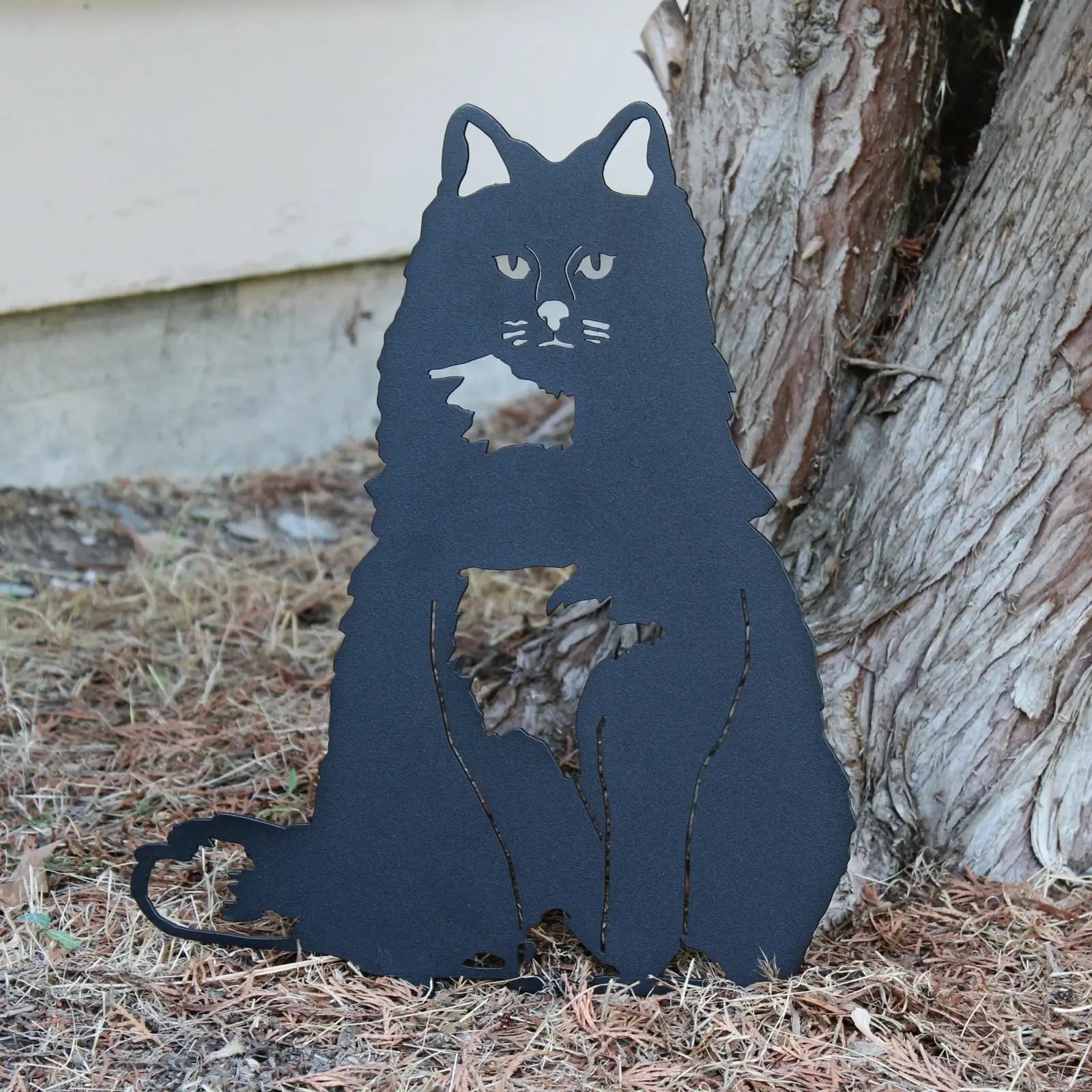 Black metal silhouette of a British Longhair cat, showcasing detailed features, set against a natural background.