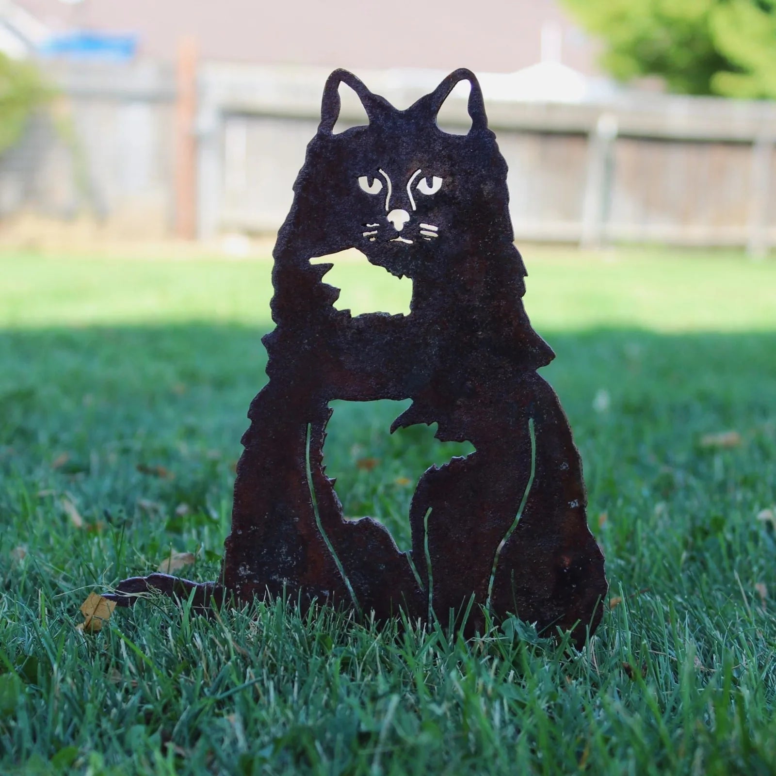 Rusty metal silhouette of a British Longhair cat, showcasing detailed cutouts, set against a grassy outdoor backdrop.