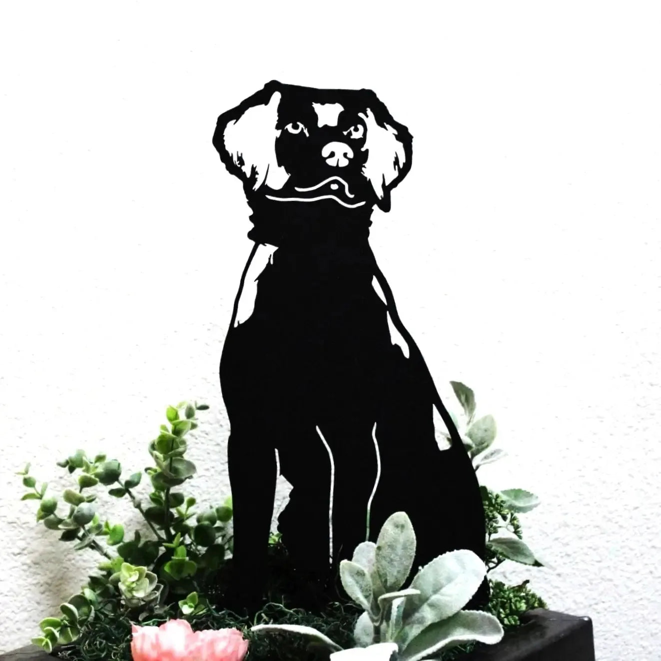 Silhouette of a Brittany Spaniel in black metal, surrounded by green foliage and flowers, showcasing outdoor decor style.