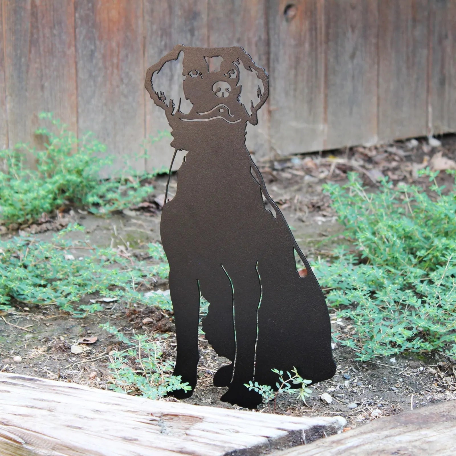 Black metal silhouette of a Brittany Spaniel sitting among green plants, designed for outdoor dog decor.