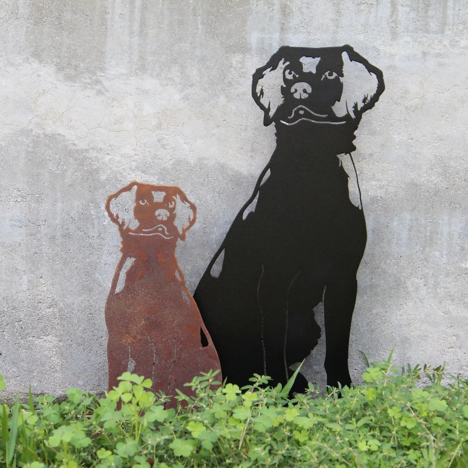 Rusty Corten steel and matte black metal silhouettes of Brittany Spaniel dogs, set against a textured wall and greenery.