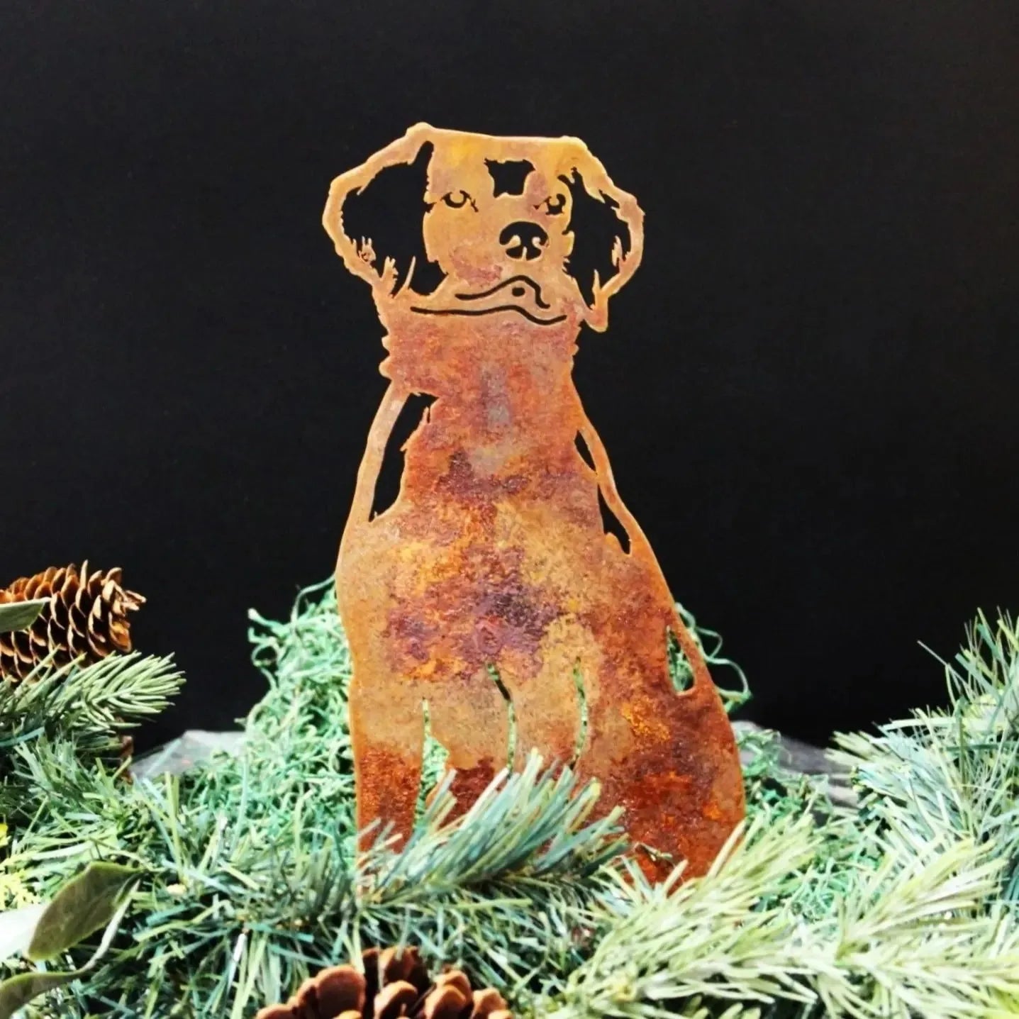 Rusty metal silhouette of a Brittany Spaniel dog, surrounded by greenery and pinecones, perfect for outdoor decor.