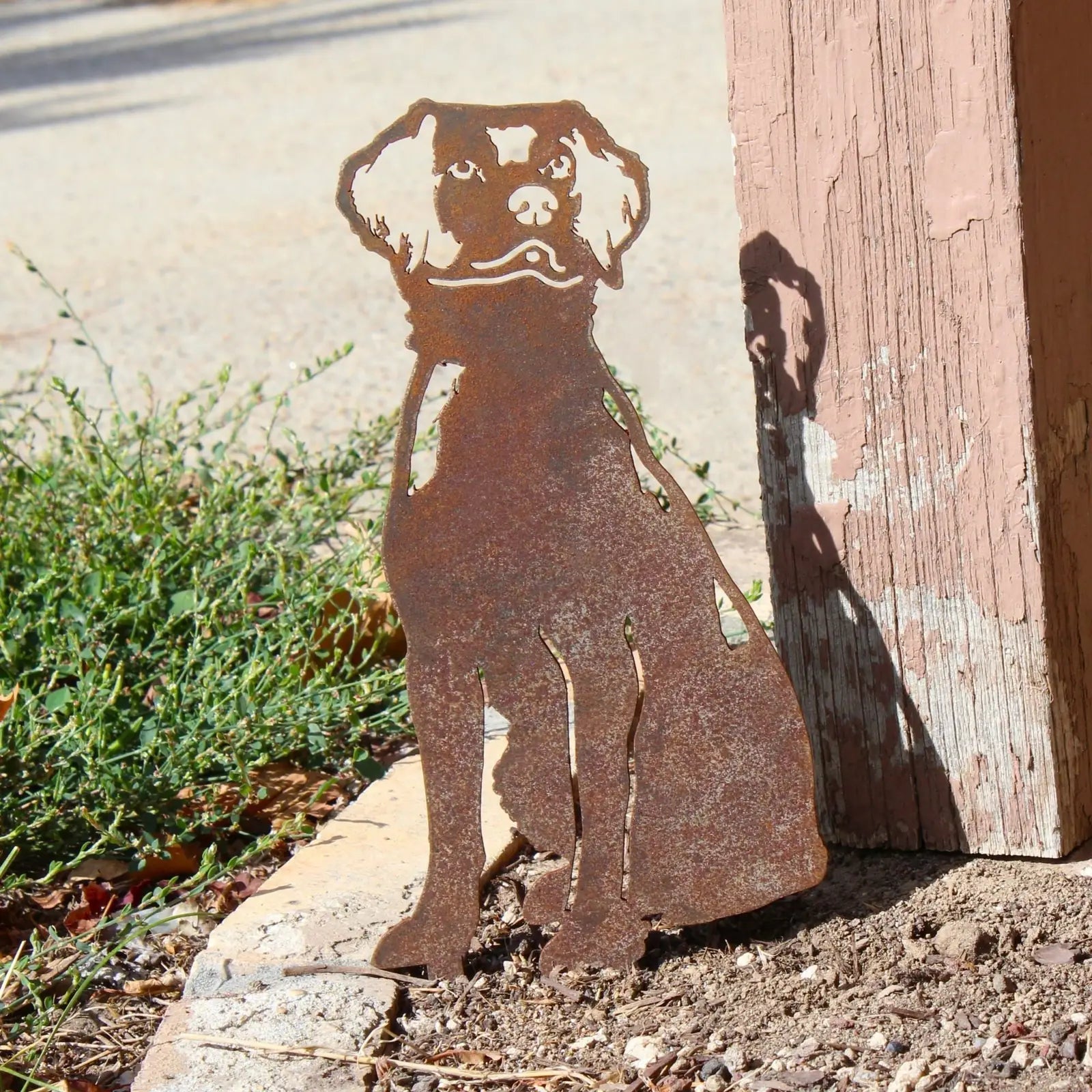 Rusty metal silhouette of a Brittany Spaniel dog, positioned among green plants, ideal for outdoor decor.
