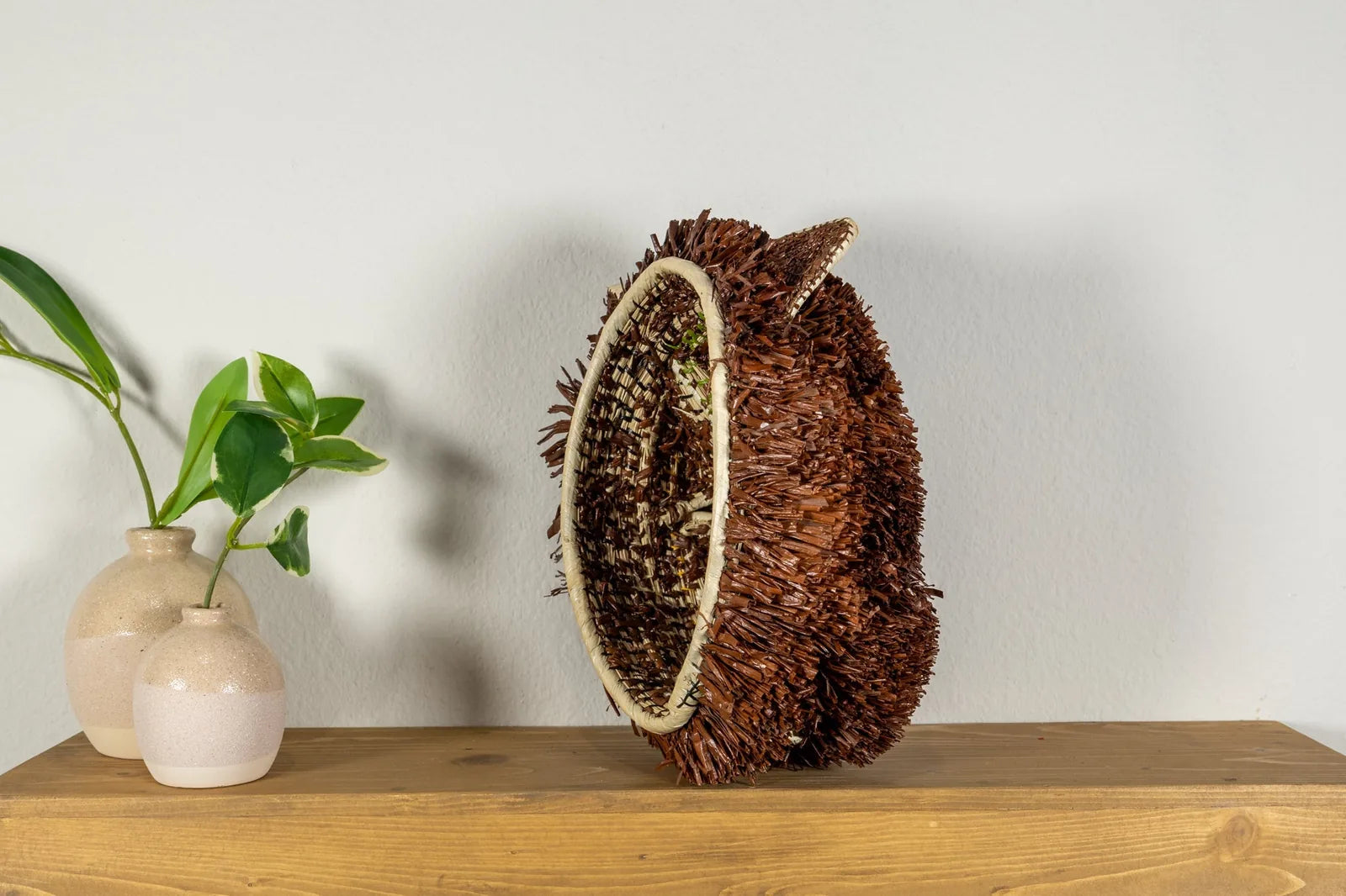 Handwoven brown and white Labradoodle dog mask displayed on a wooden table with ceramic vases and plants.