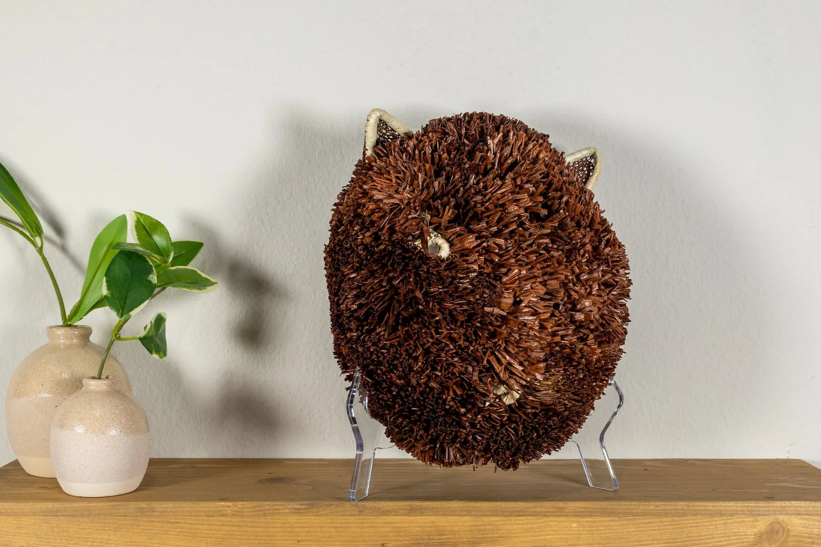 Handwoven brown and white Labradoodle dog mask, crafted from natural reeds, displayed on a wooden shelf with decorative va...