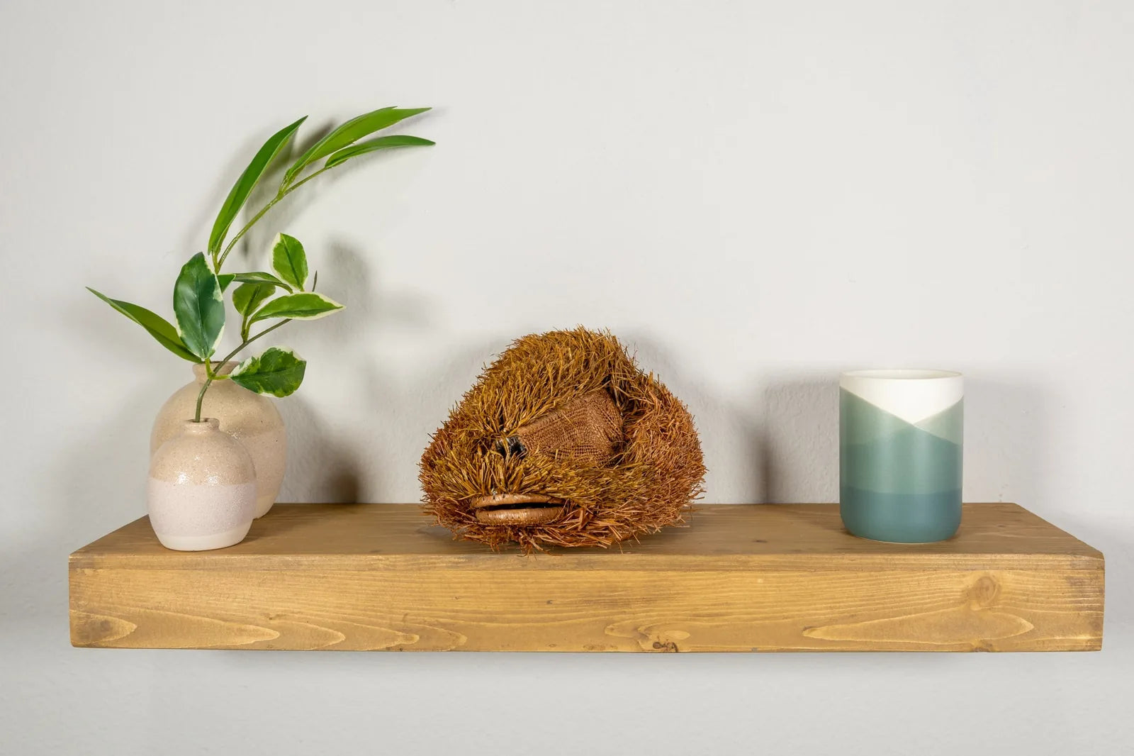 Handwoven brown Labradoodle dog mask with intricate textures, displayed on a wooden shelf alongside vases and a candle.