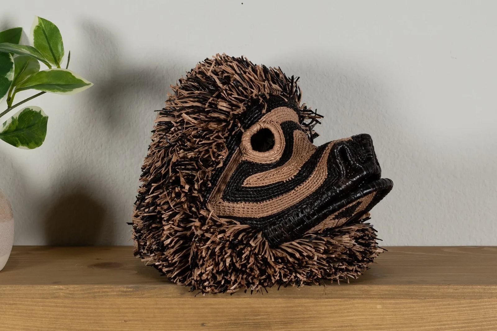 Handwoven brown poodle dog mask with intricate patterns, featuring natural colors and textured fringe, displayed on a wood...