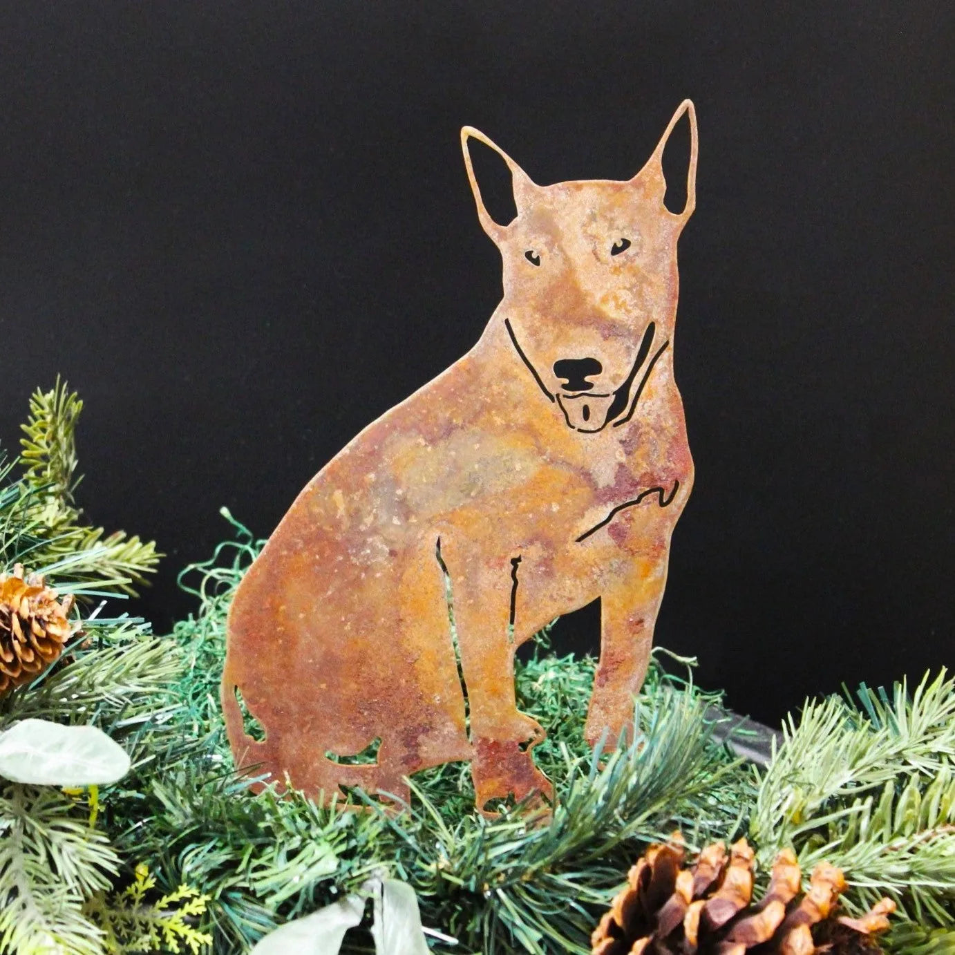 Bull Terrier silhouette in rusty Corten steel, set amidst greenery and pine cones, perfect for outdoor decor.