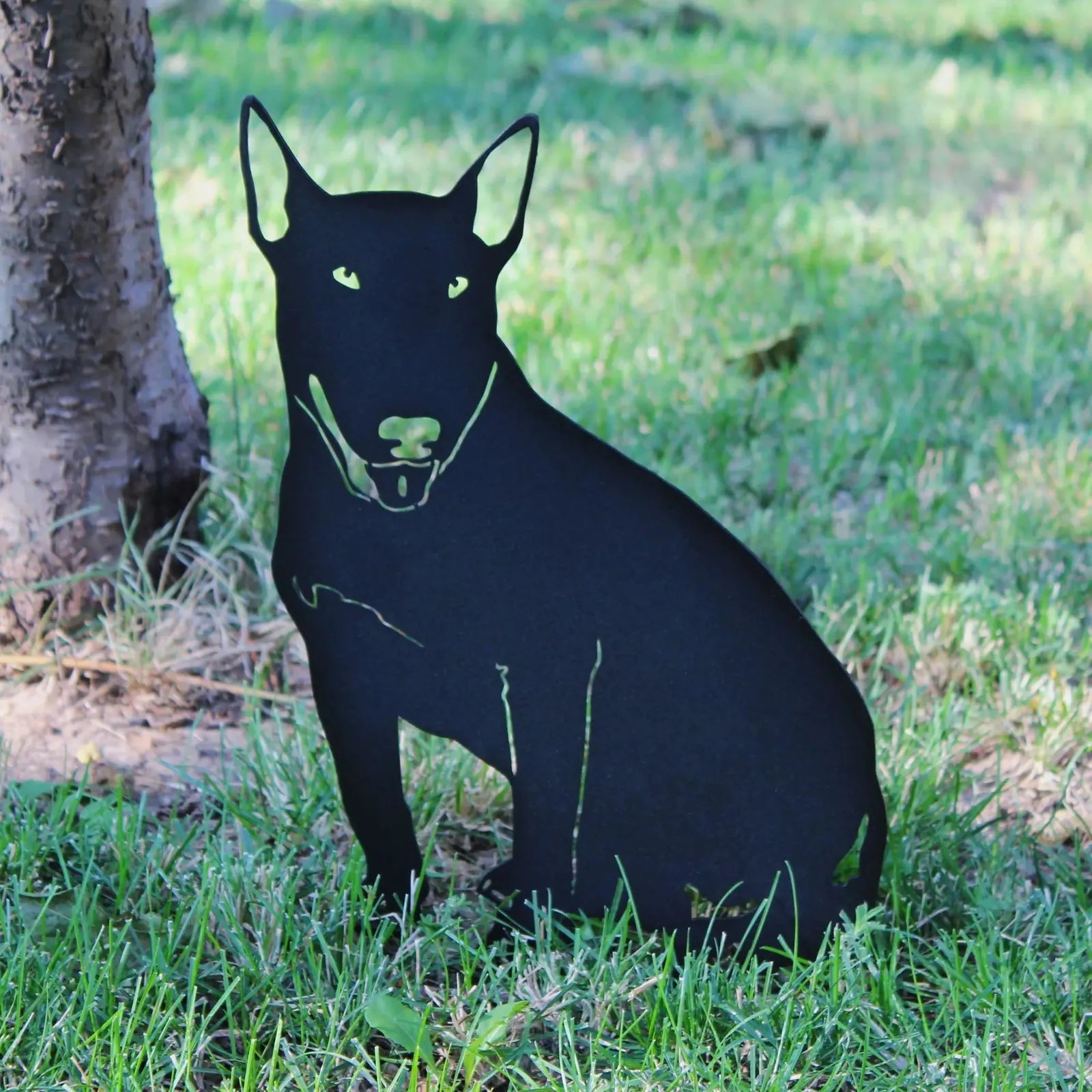 Black Bull Terrier metal silhouette sitting on grass, showcasing a sleek design, perfect for garden decor.