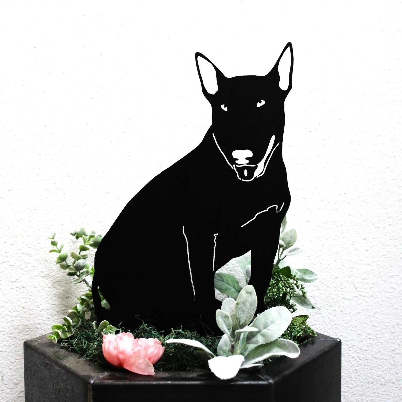 Black Bull Terrier metal silhouette art surrounded by decorative greenery and a pink flower, showcasing sturdy craftsmanship.