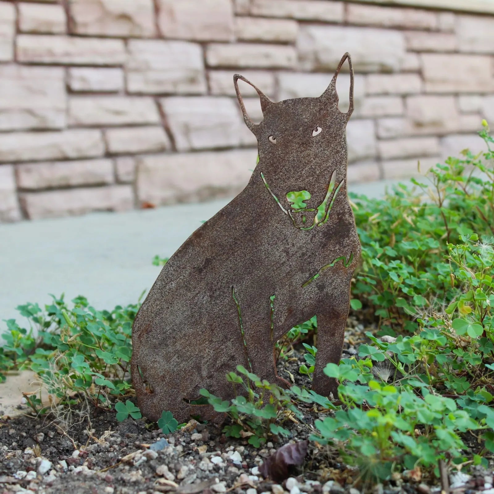 Bull Terrier metal silhouette in weathered Corten steel, integrated into greenery for outdoor decor.