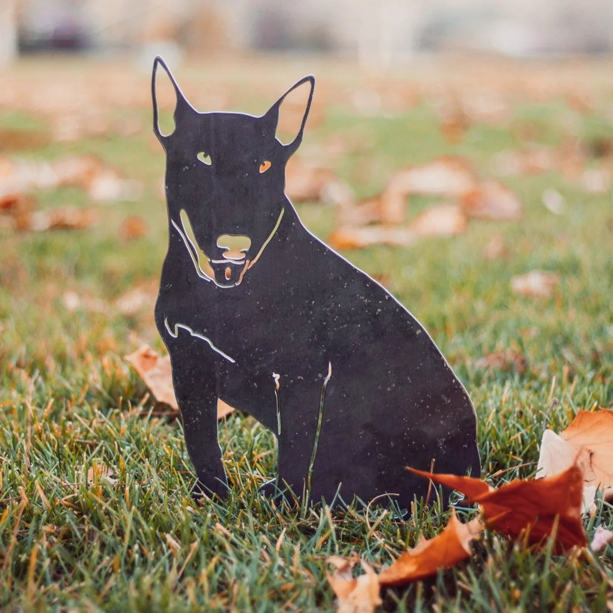 Black Bull Terrier metal silhouette standing among grass and fallen leaves, showcasing a sleek design for garden decor.