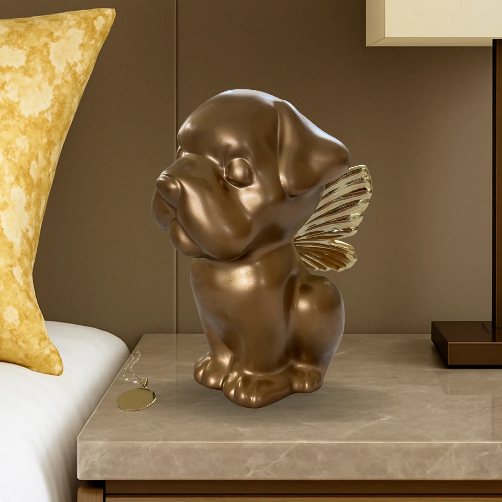 Gold Bully Angel dog urn with wings, sitting on a bedside table beside a yellow pillow and lamp.