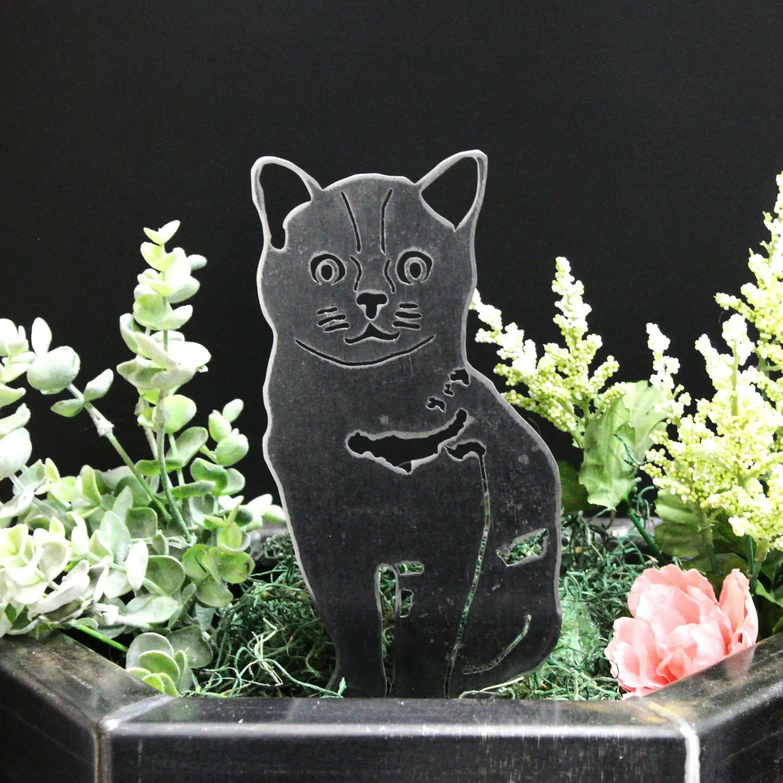 Black Burmese metal silhouette in a planter, surrounded by greenery and flowers, showcasing a cat design.