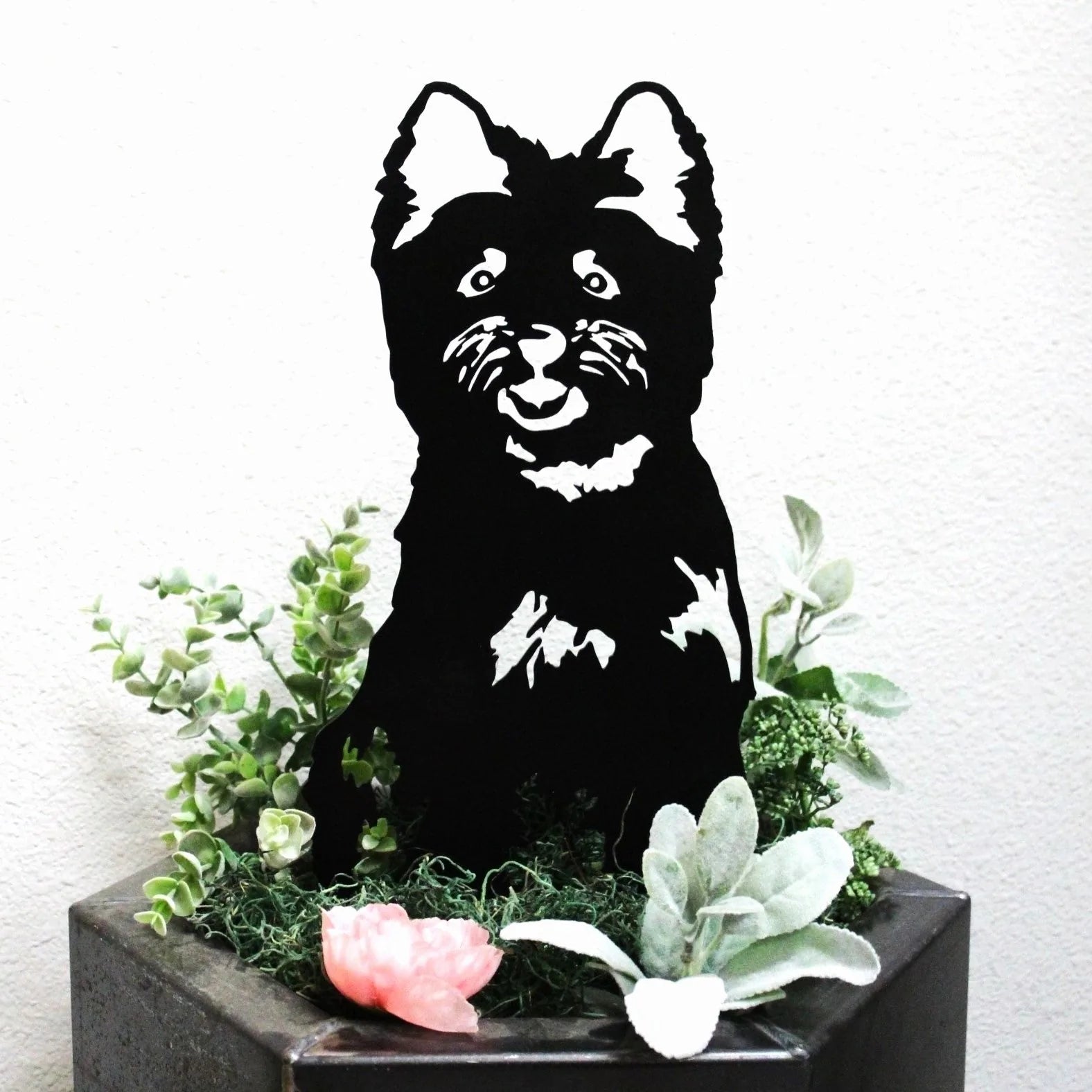 Cairn Terrier silhouette in black metal, surrounded by green foliage and decorative elements.