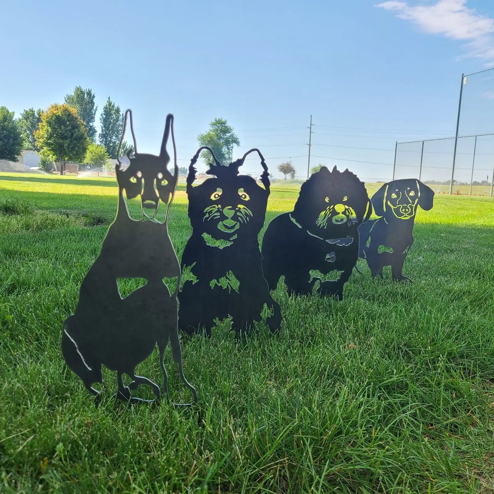 Cairn Terrier silhouette in black metal alongside other dog breed art pieces on green grass.