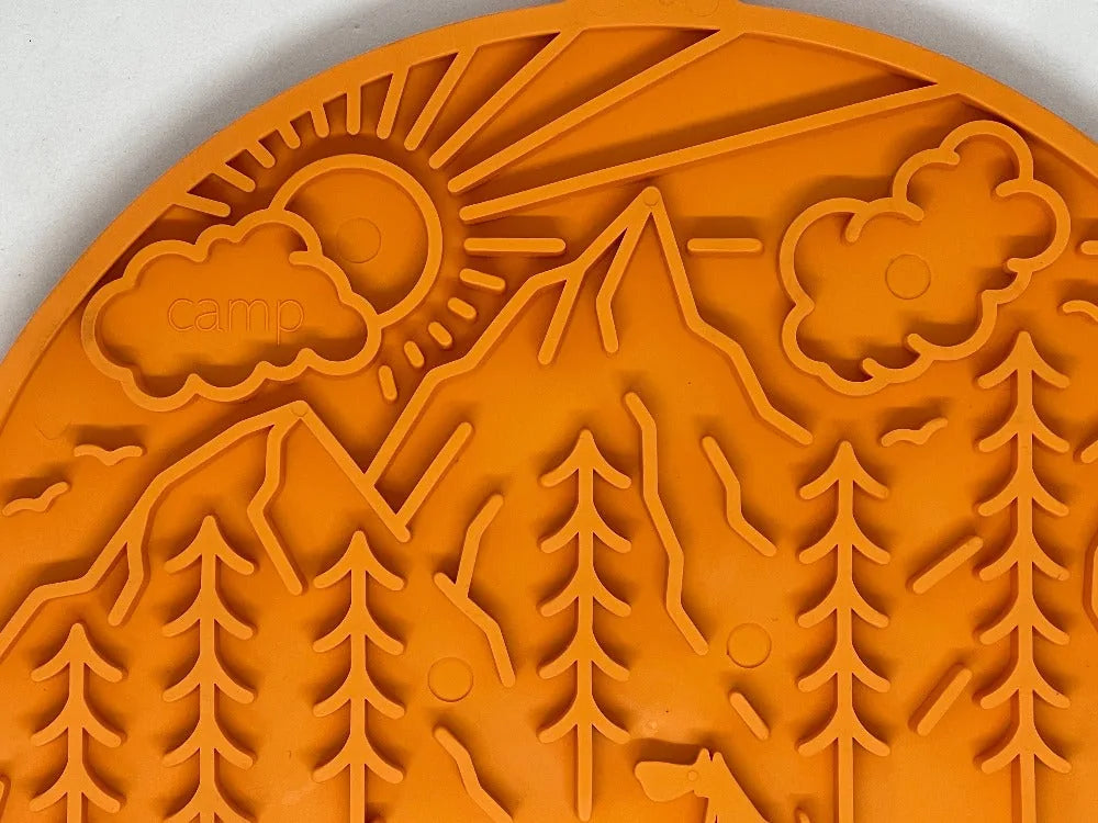 Bright orange lick mat featuring a retro camper van design, textured mountains, and trees, perfect for enriching playtime.