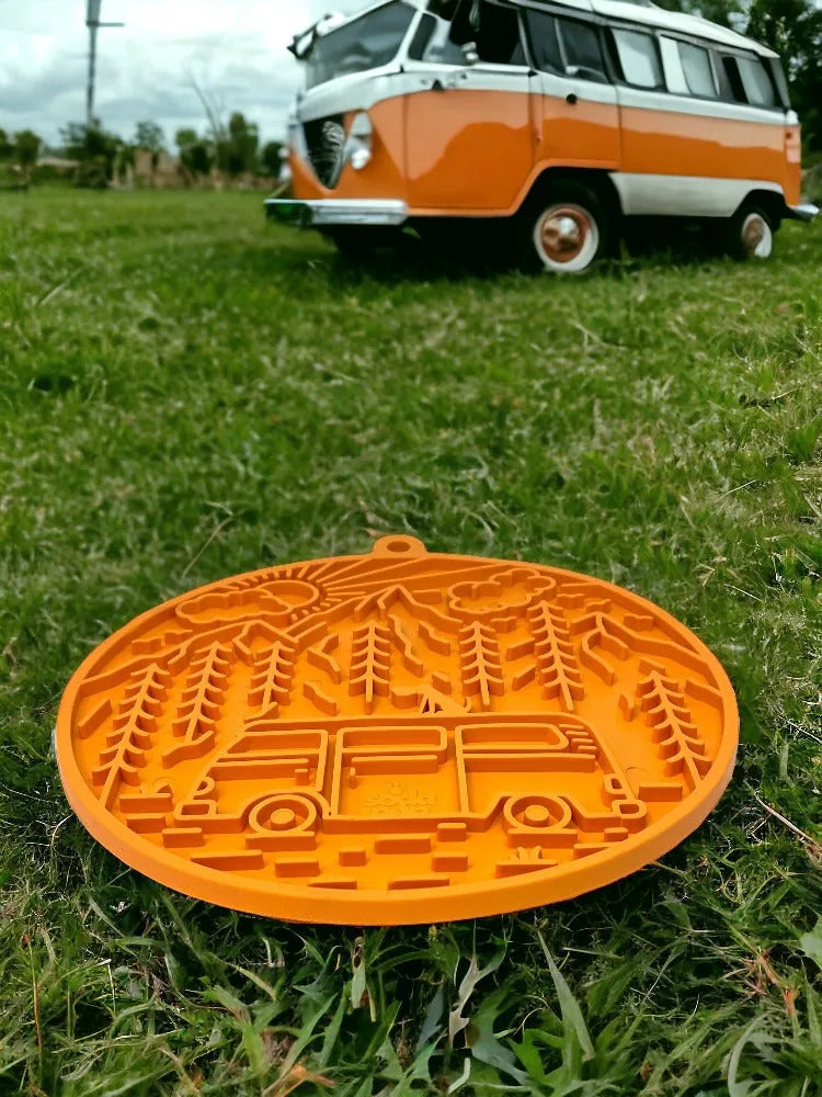 Orange Camp eMat with retro camper van design, textured surface, and suction cups, resting on grass with a vintage van in...