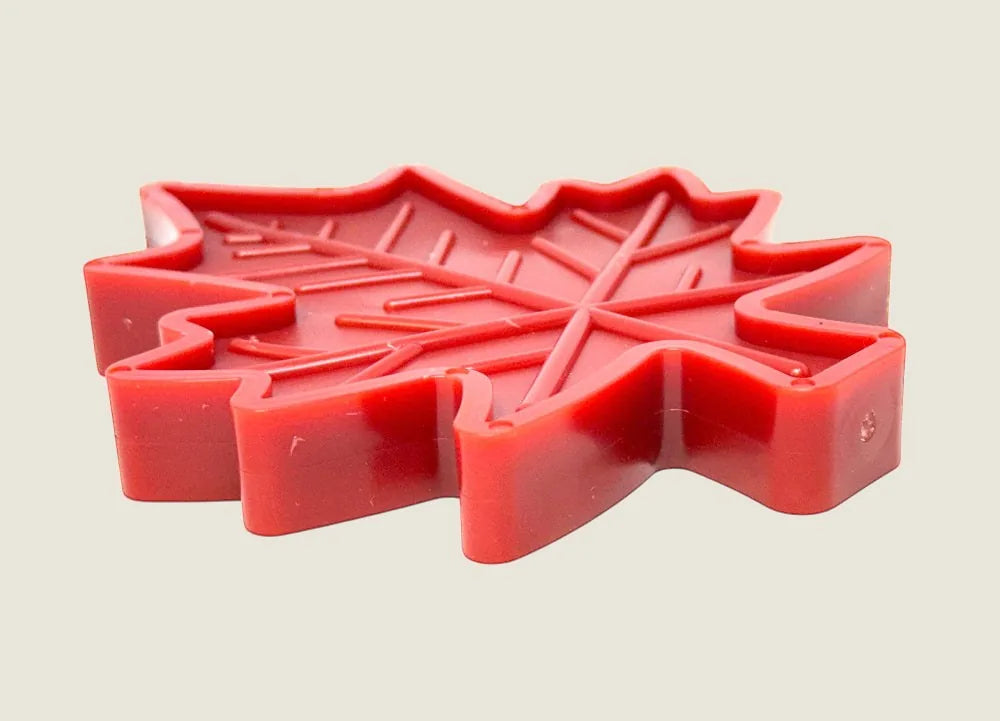 Red Canadian maple leaf-shaped nylon dog chew toy with textured grooves for treat stuffing, made in the USA.