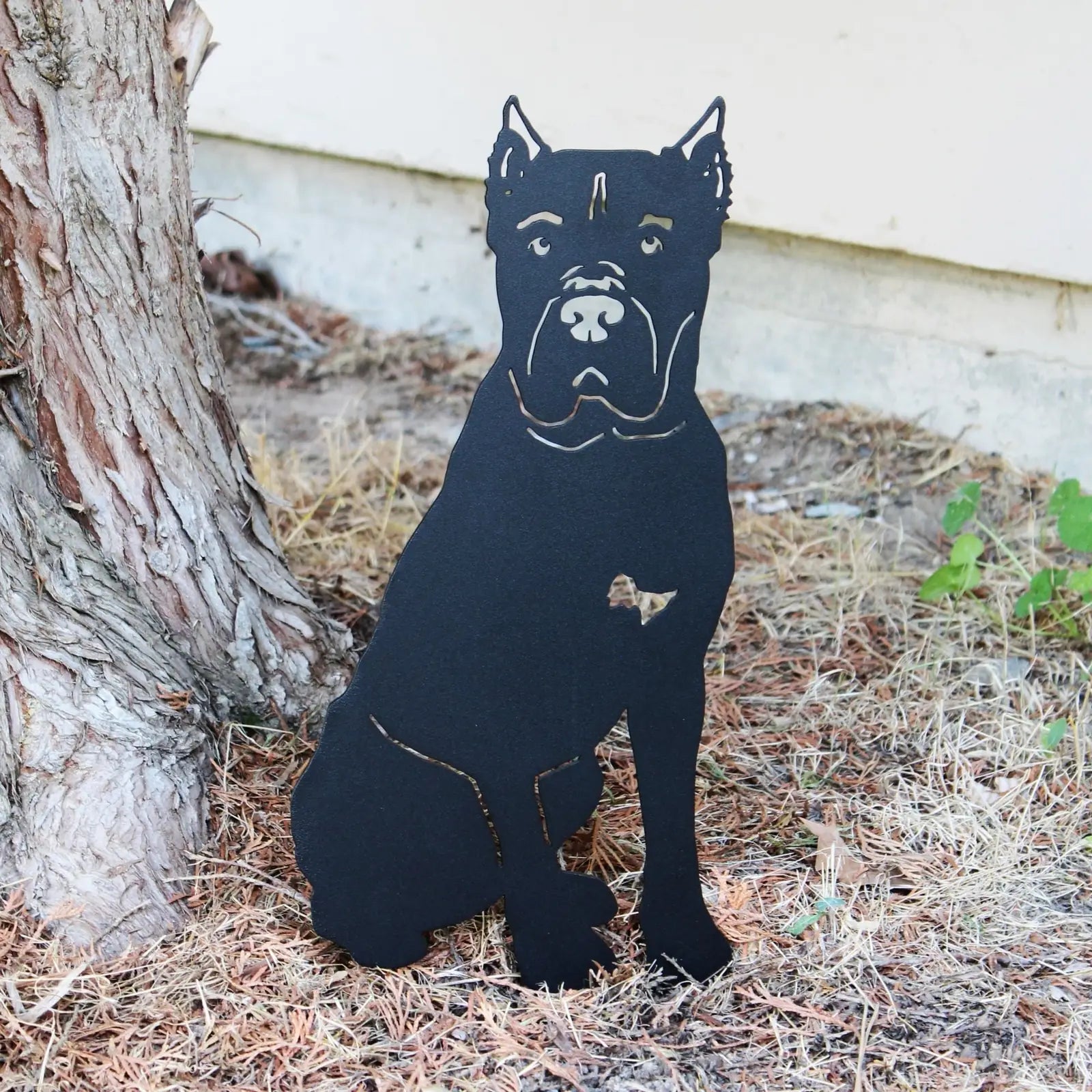 Black metal silhouette of a Cane Corso sitting next to a tree, showcasing an outdoor decor accent made from sturdy material.