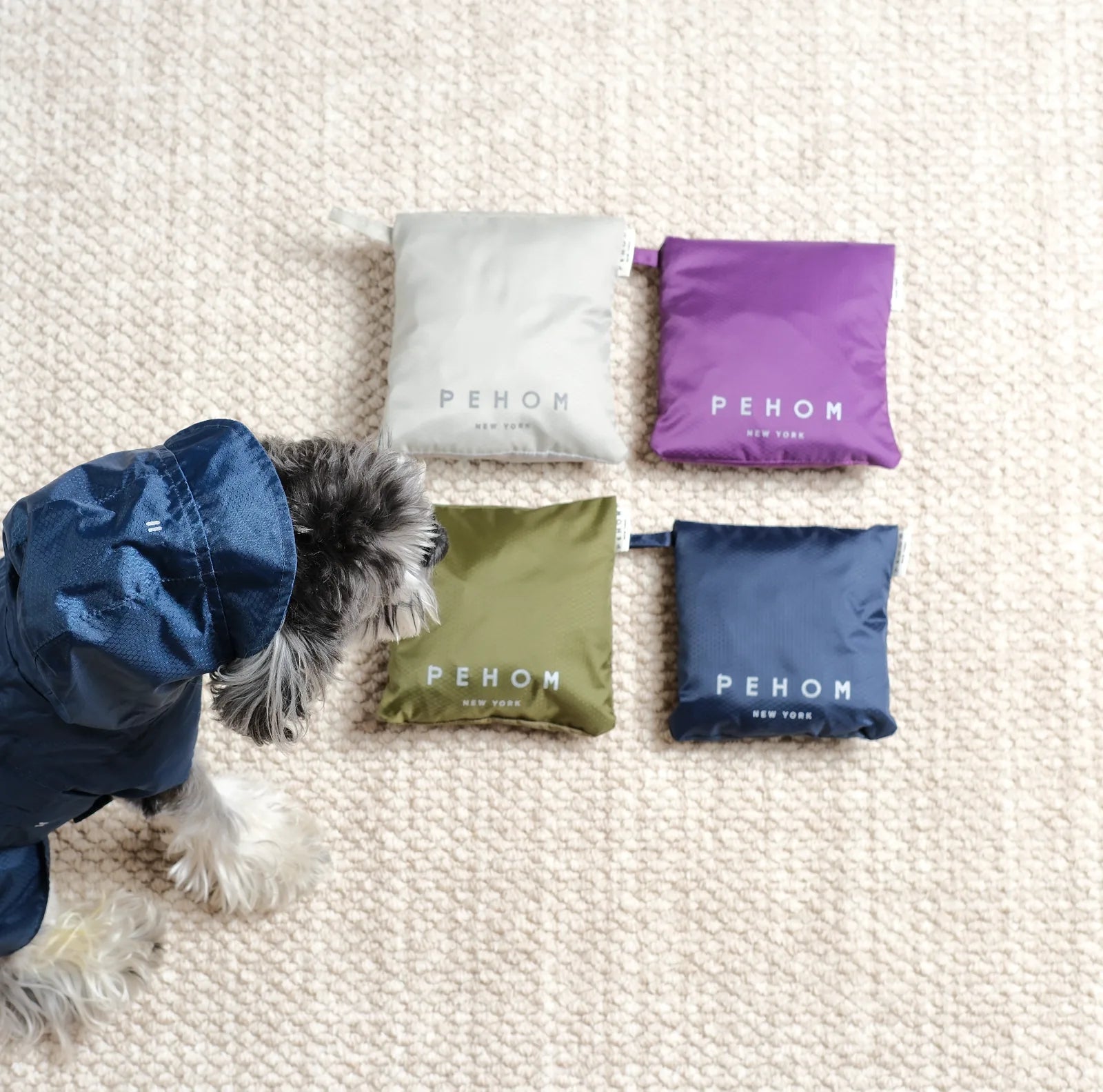 Purple raincoat for dogs beside folded raincoats in gray, green, and navy, demonstrating lightweight and compact design.