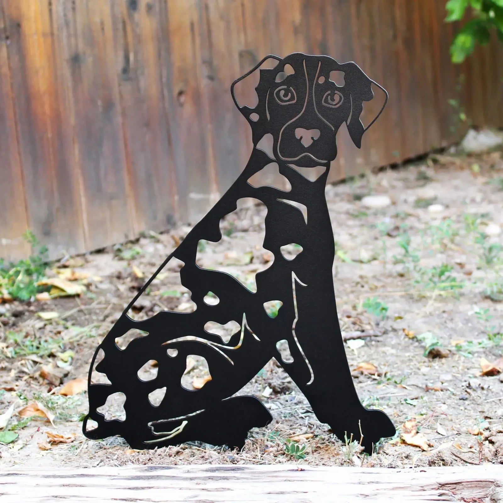 Black metal silhouette of a Catahoula Leopard Dog featuring cut-out patterns, positioned in a rustic outdoor setting.
