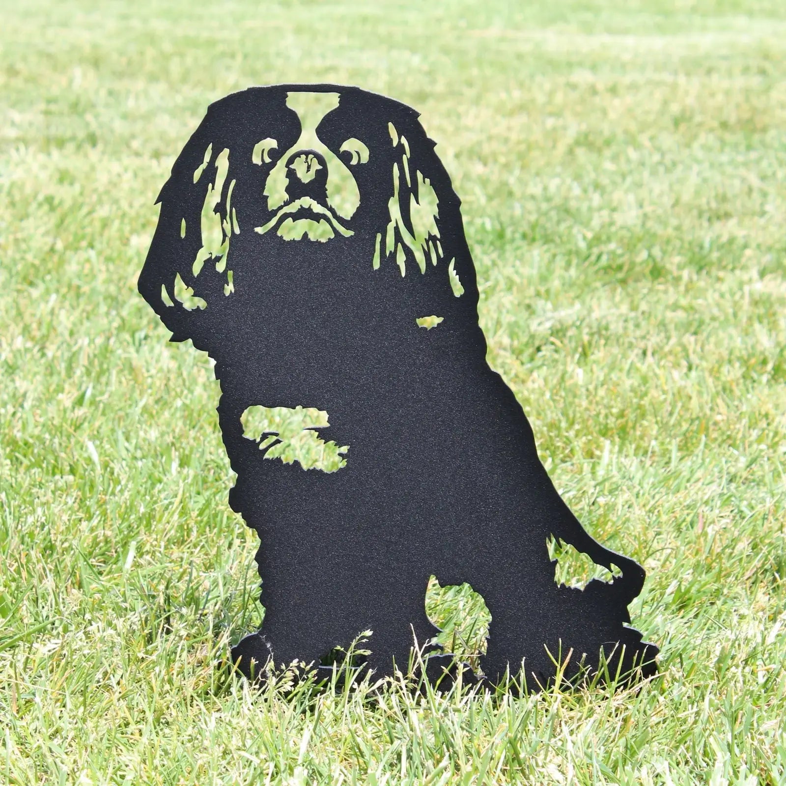 Black metal silhouette of a Cavalier King Charles Spaniel, standing in grass, showcasing intricate cut-out details.