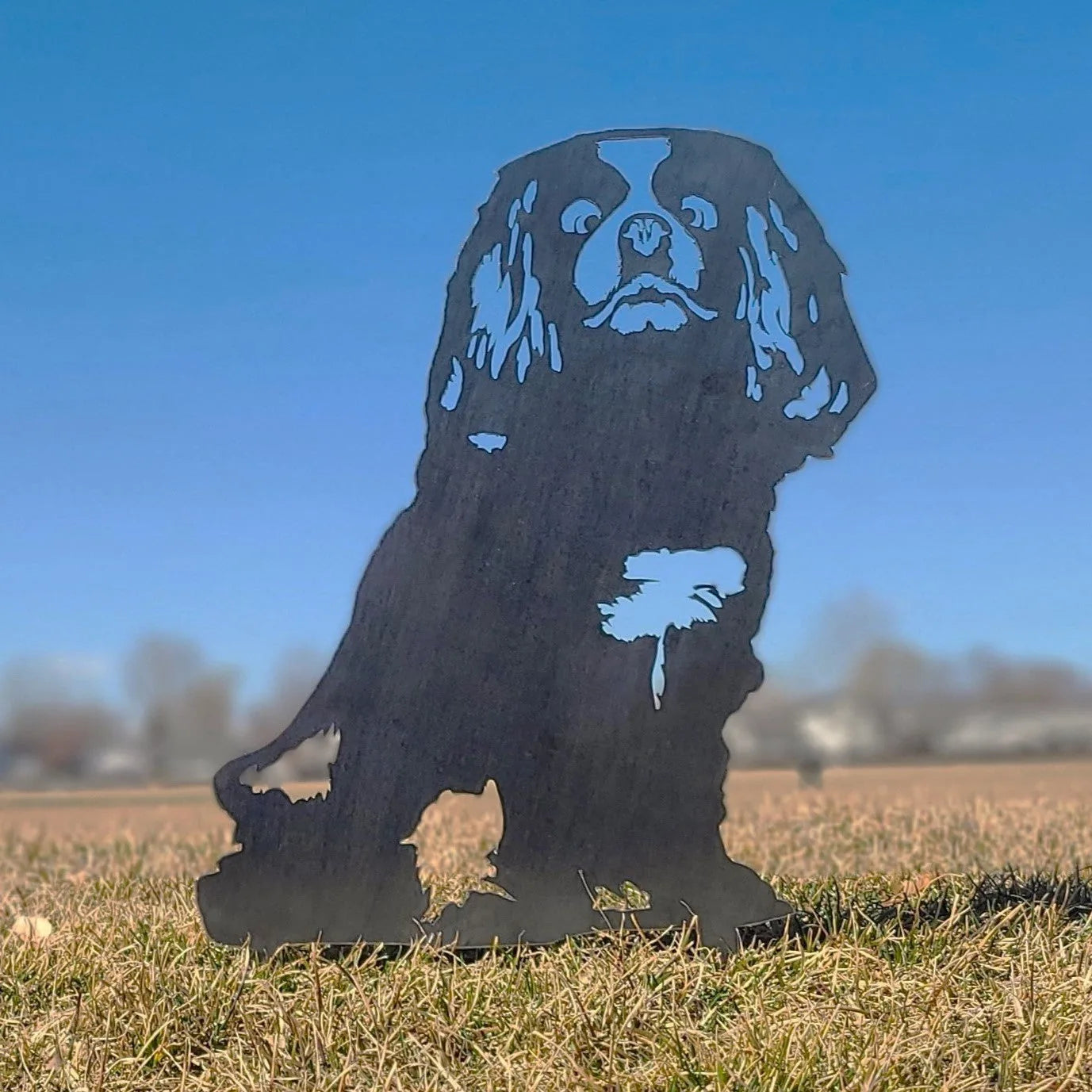 Cavalier King Charles Spaniel silhouette in weathering steel, displayed outdoors against a clear blue sky.