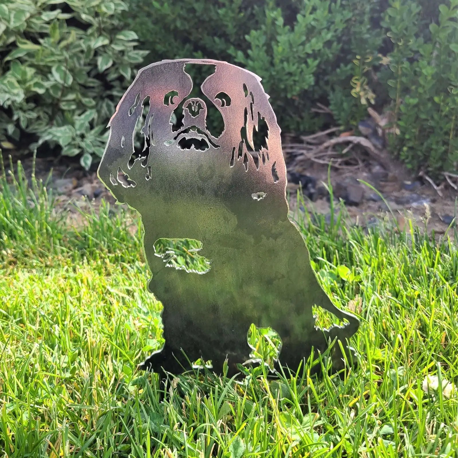 Cavalier King Charles Spaniel metal silhouette in weathered steel, standing on green grass against a blurred backdrop.