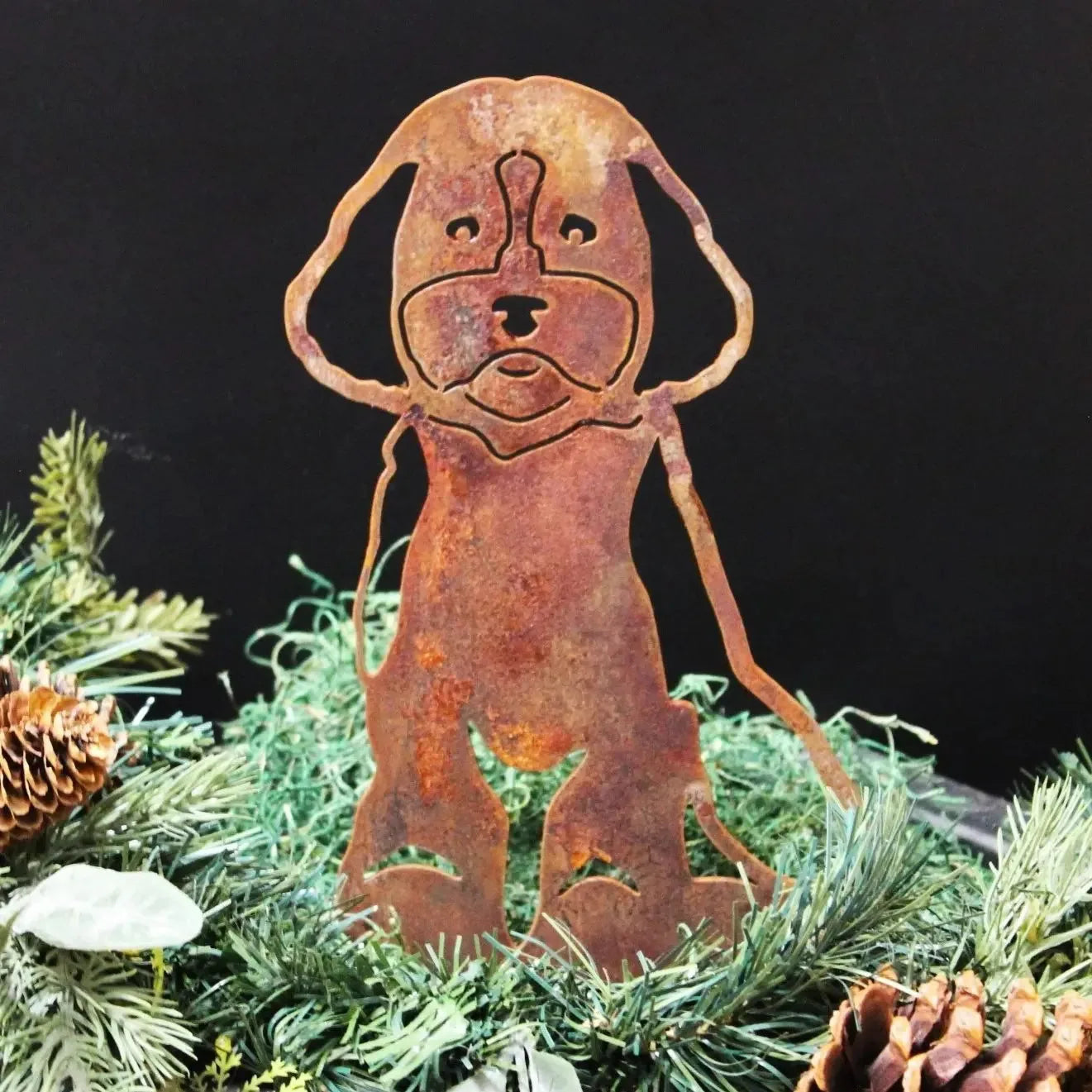 Rusty Cavapoo metal silhouette standing among evergreen foliage and pinecones, showcasing a weathered Corten steel finish.