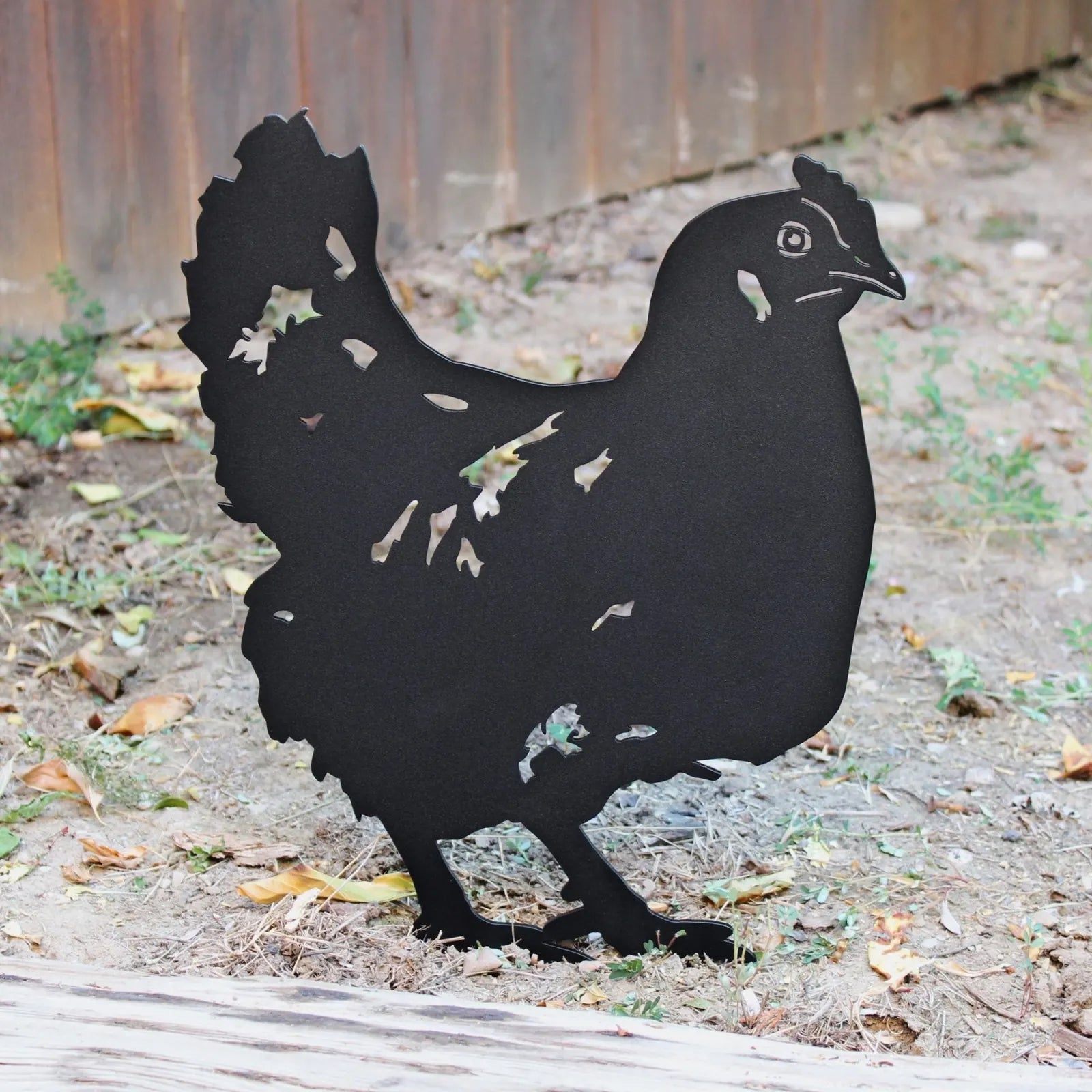 Black metal chicken silhouette standing on the ground, showcasing intricate cut-out details, perfect for garden decor.